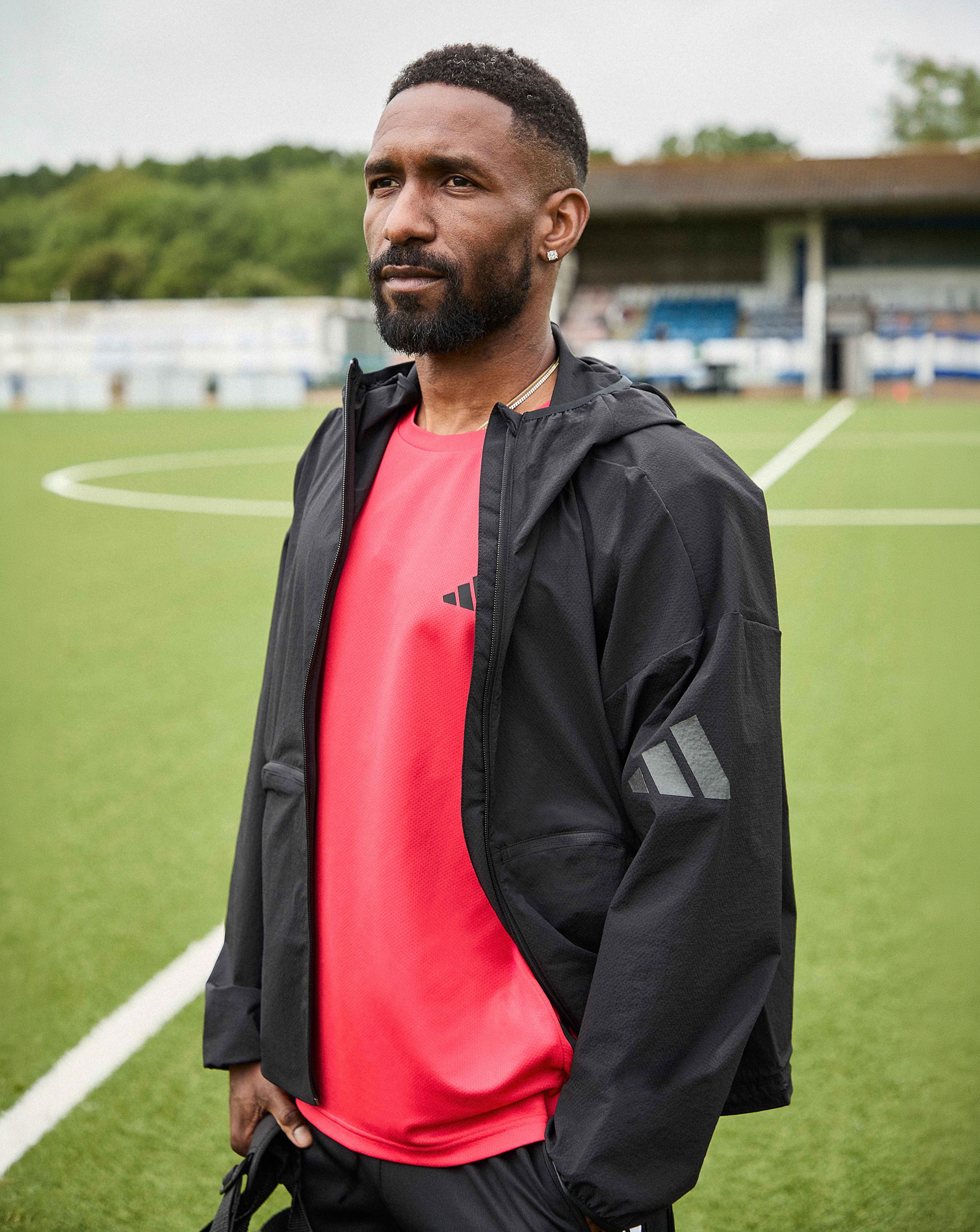 Jermain Defeo is wearing a red adidas workout essentials training t-shirt underneath a black adidas Myshelter wind cheater jacket.