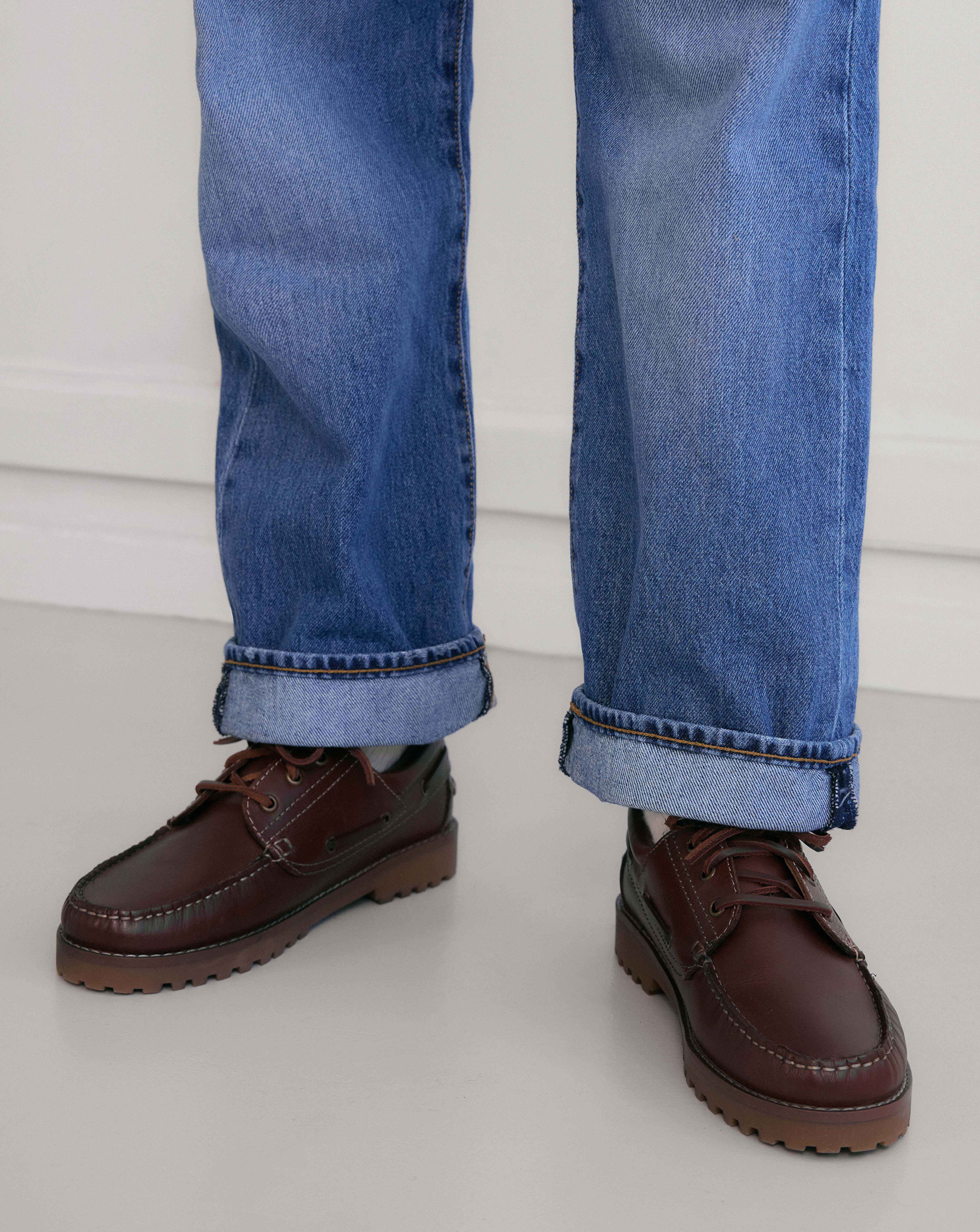 Model is wearing a pair of dark brown boat shoes with a pair of denim jeans.