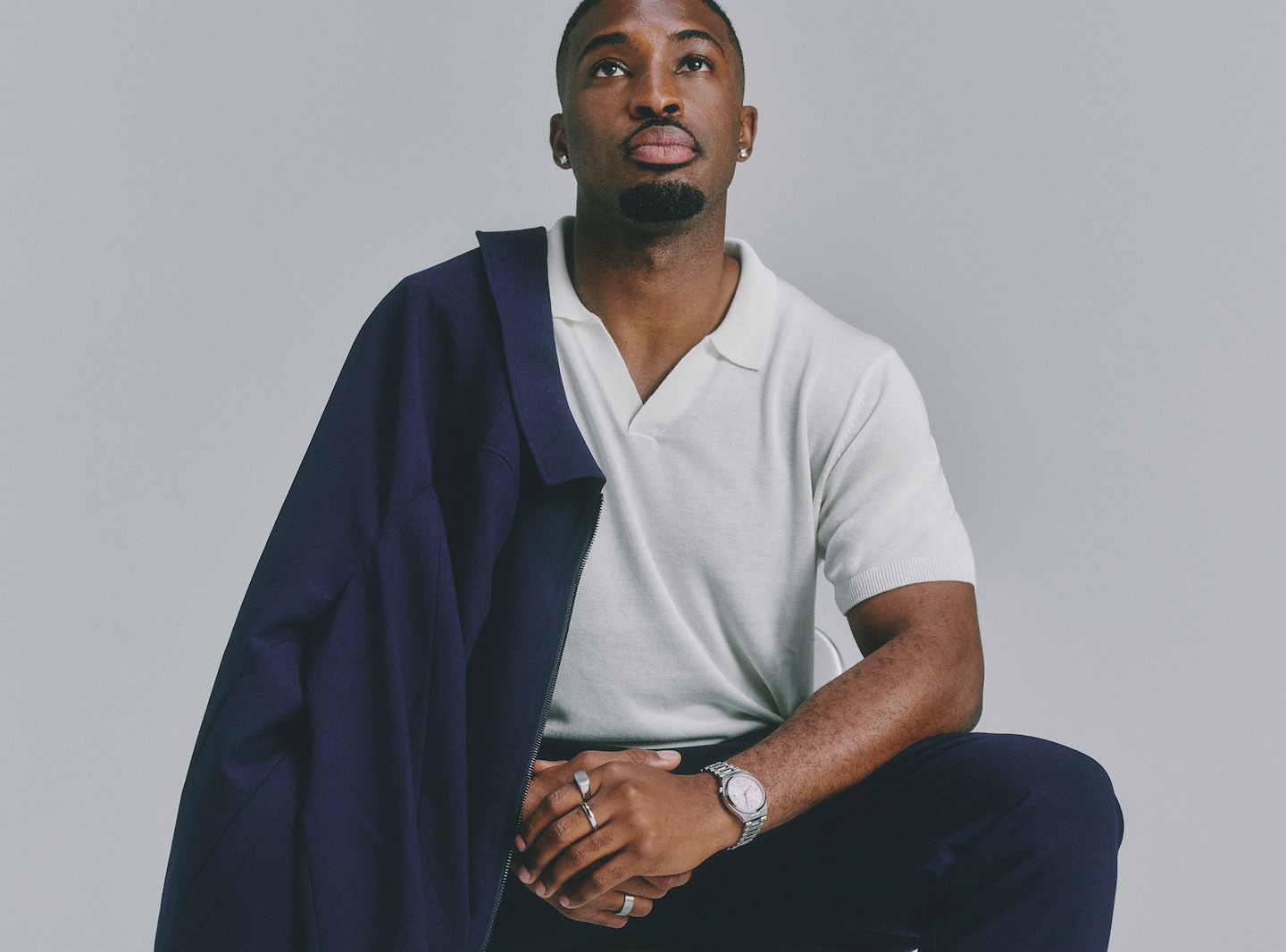 Model wears knitted polo in white with navy trousers and jacket