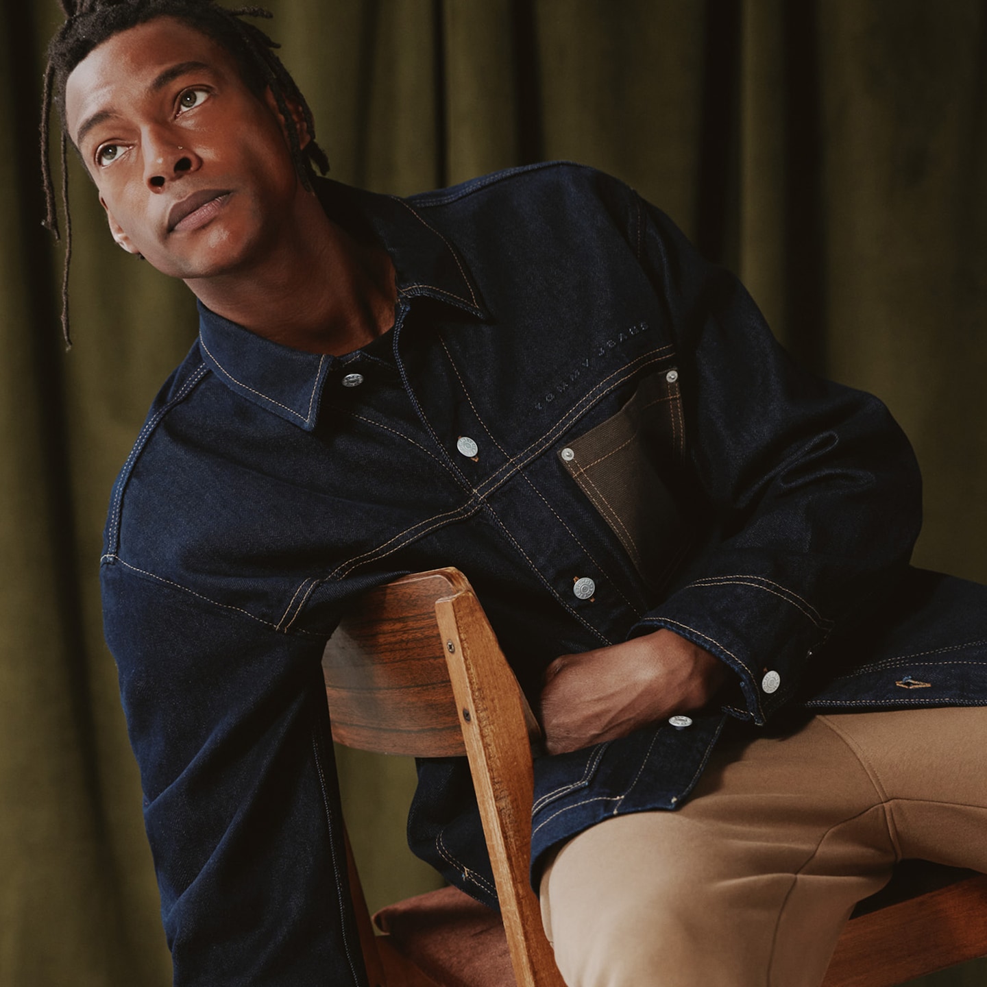 Model is wearing a dark denim Tommy Jeans Chore jacket with cream trousers.