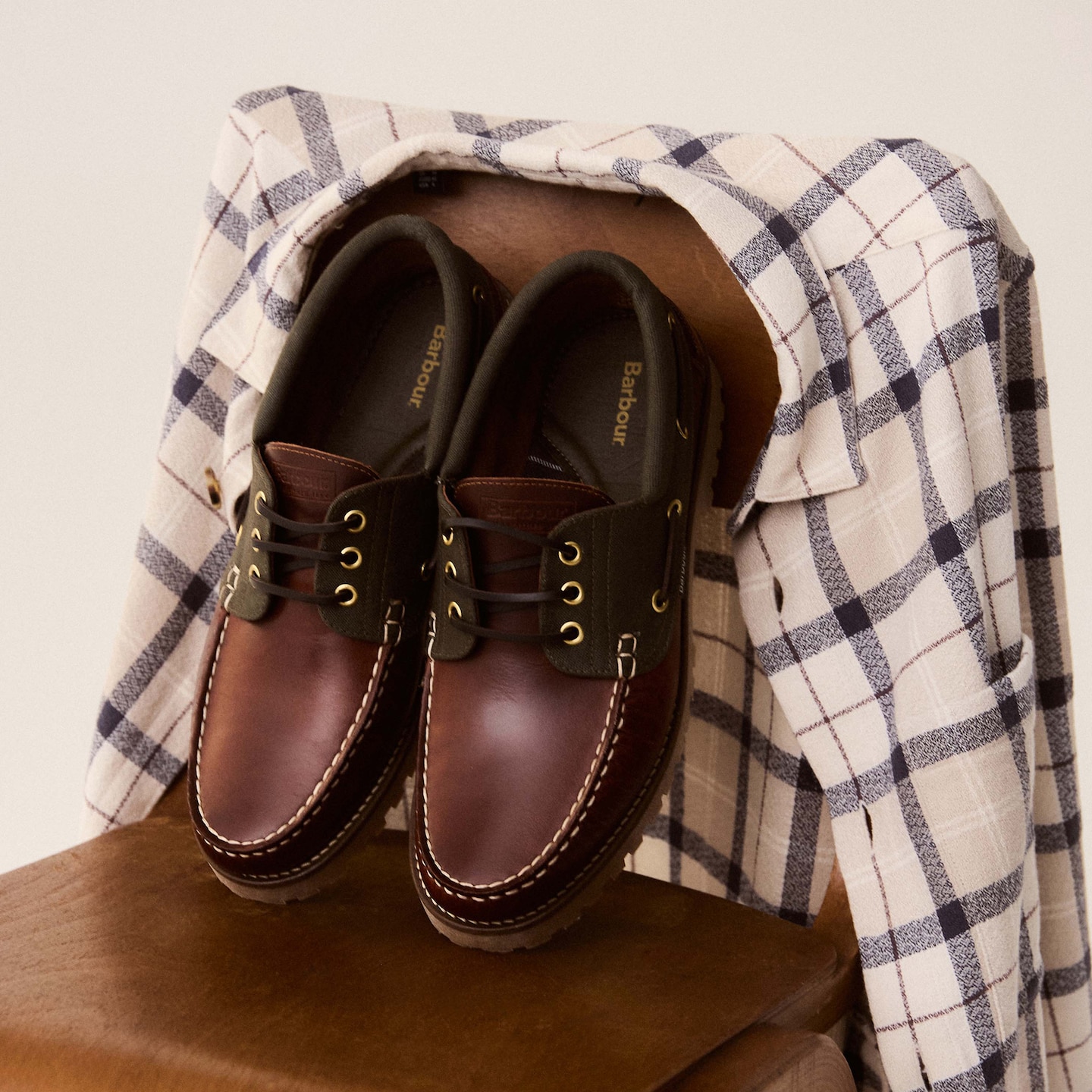 A tartan Barbour Vennel textured overshirt on the back of a chair with a pair of mahogany Barbour deck boat shoes.