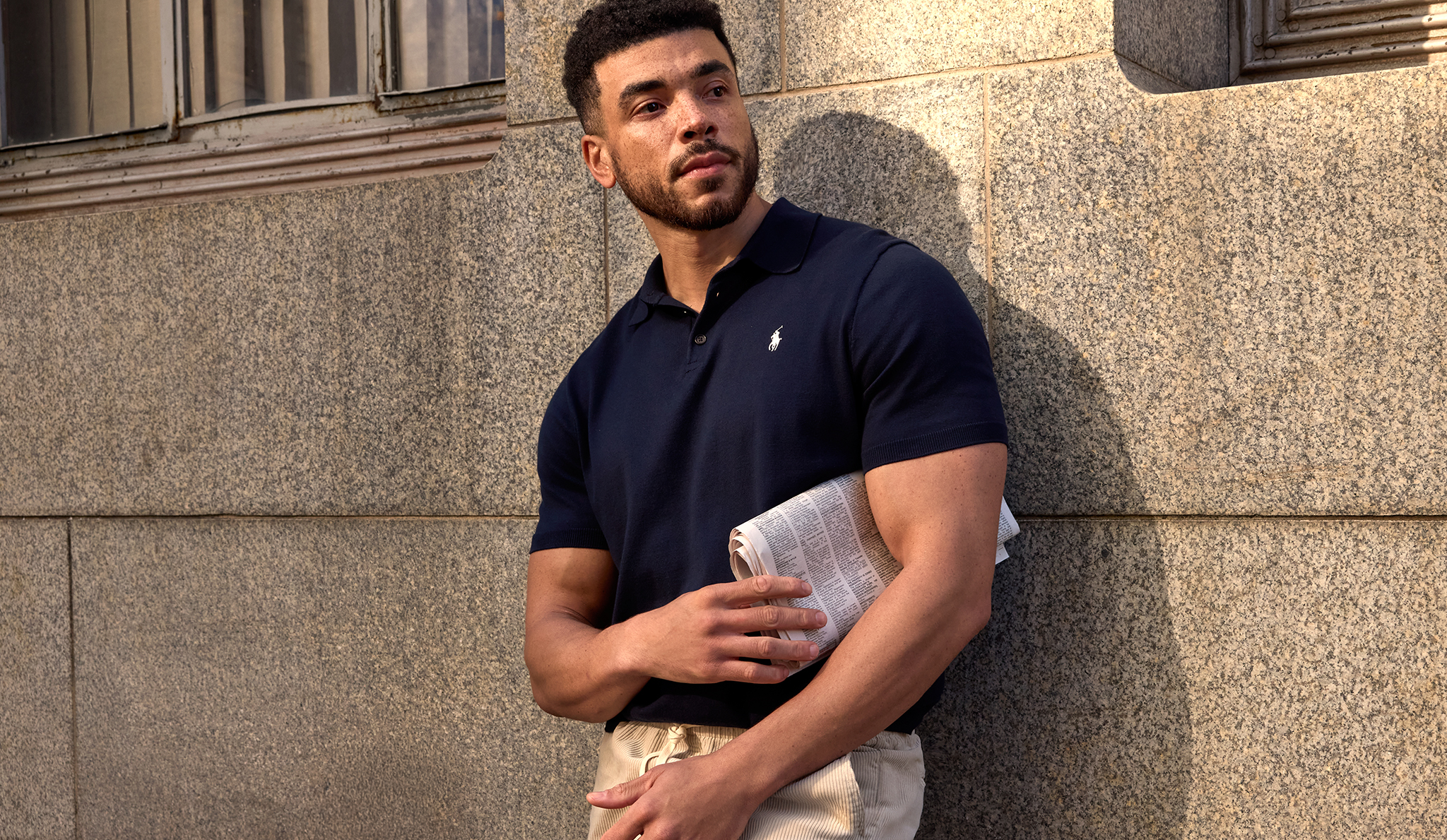 Model is wearing a navy Polo Ralph Lauren short sleeve knitted polo with beige shorts.