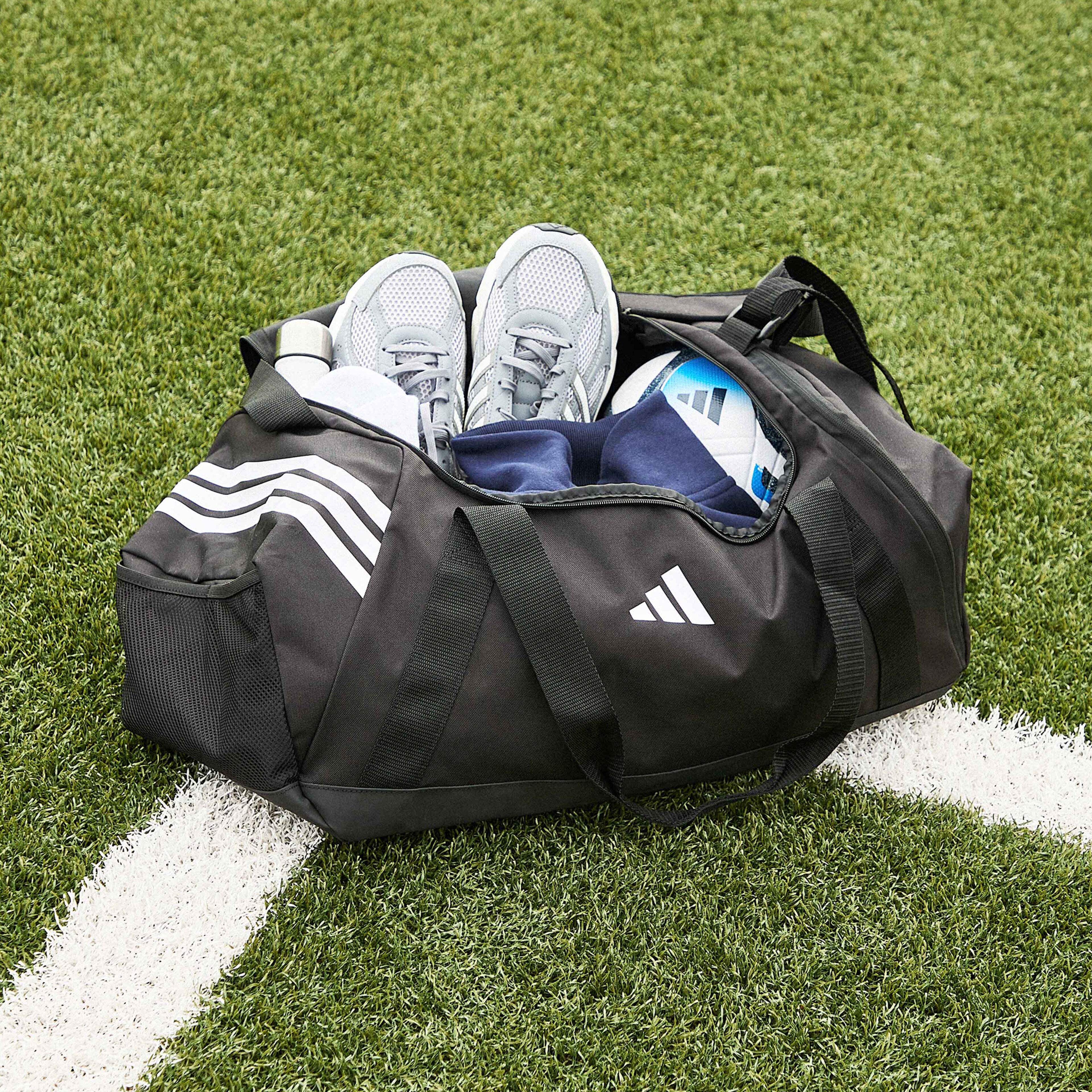 Sport mode:on. A black adidas sports bag with adidas Technochaos 2000 Trainers, a football and accessories inside.