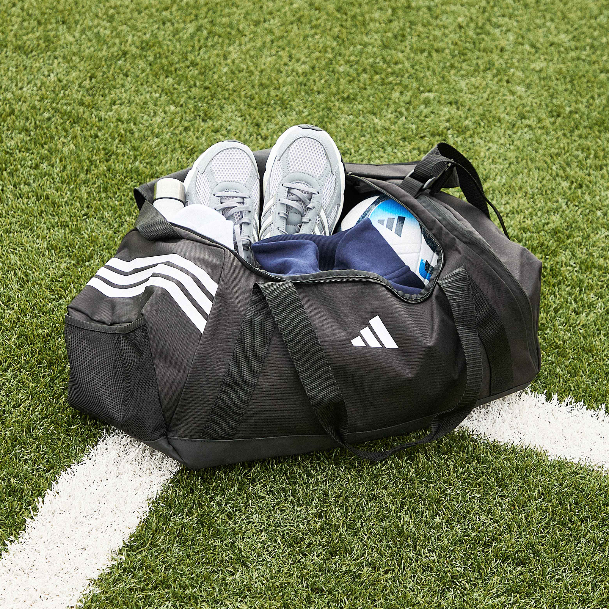 Sport mode:on. A black adidas sports bag with adidas Technochaos 2000 Trainers, a football and accessories inside.