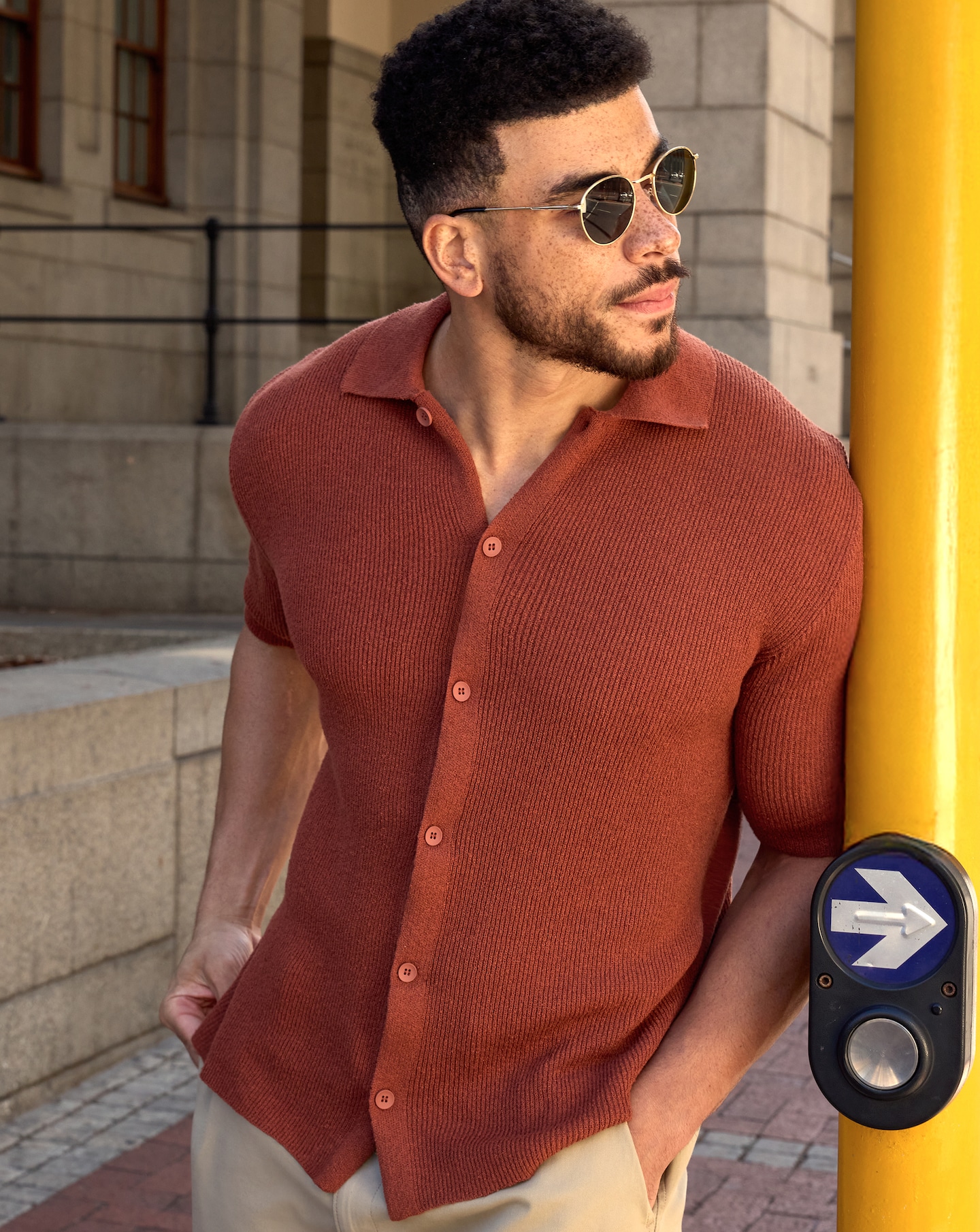 Model is wearing a rust Only & Sons Sean knitted polo with sunglasses and a pair of cream shorts.