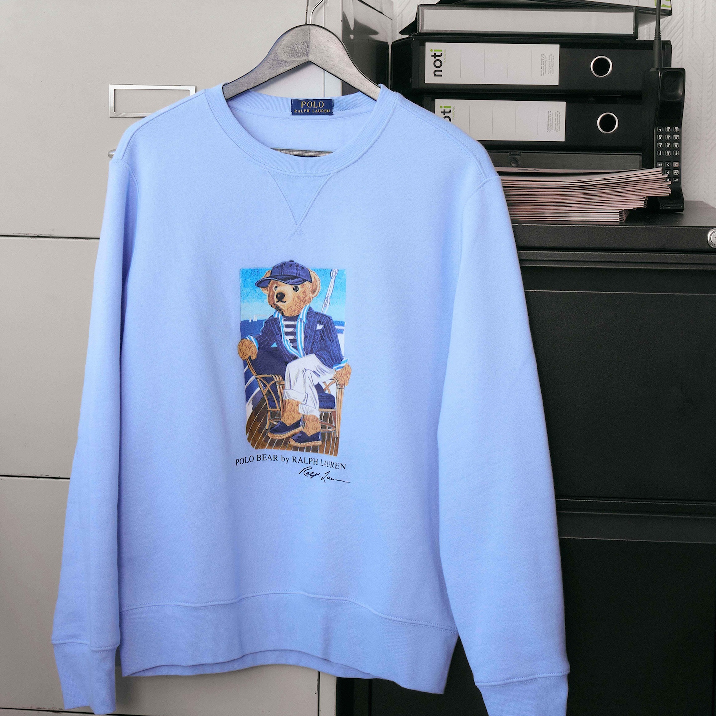 A blue Polo Ralph Lauren bear graphic crew neck sweatshirt haning on a hanger.