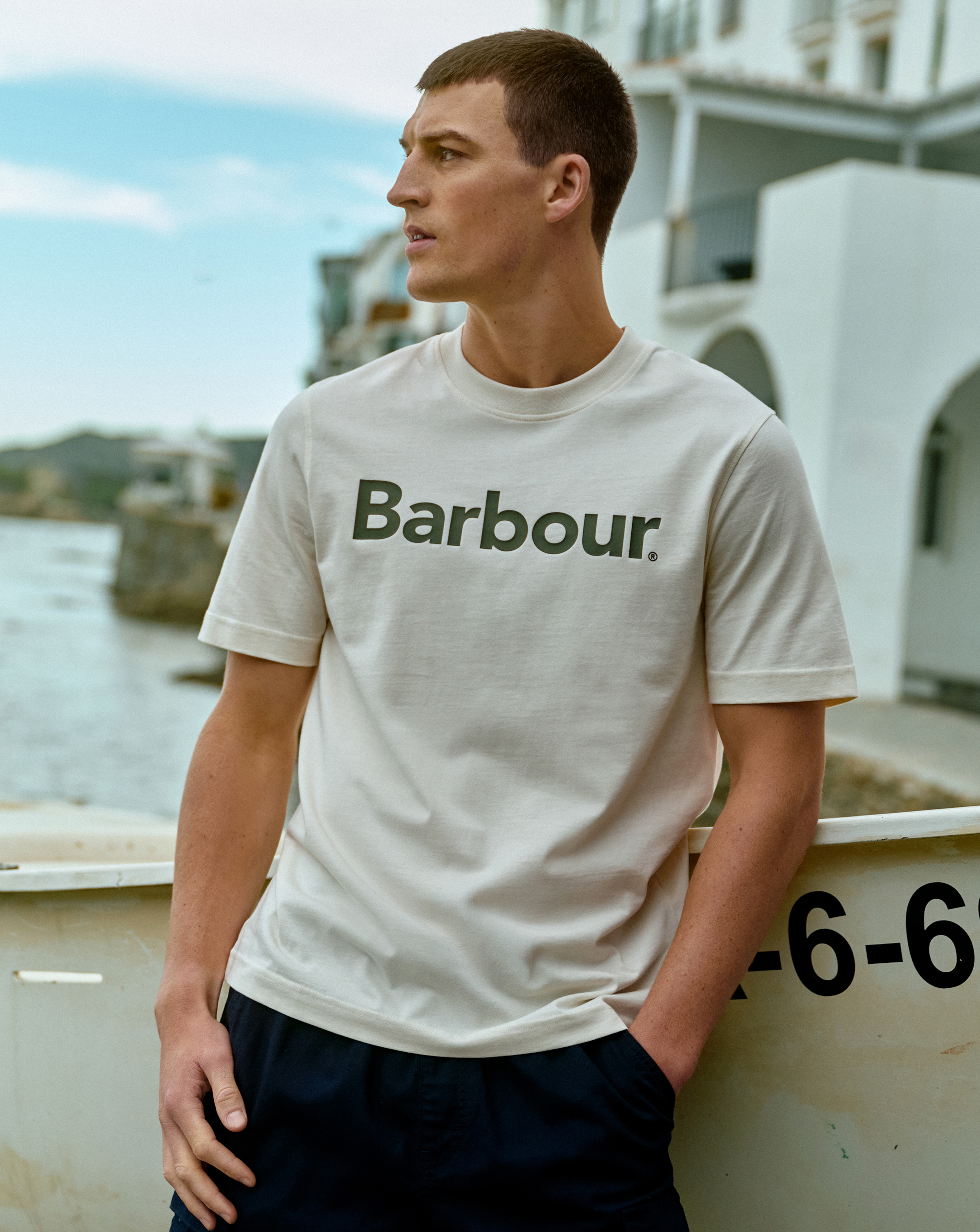 Model is wearing a white Barbour short sleeve logo relaxed t-shirt with a pair of navy shorts.