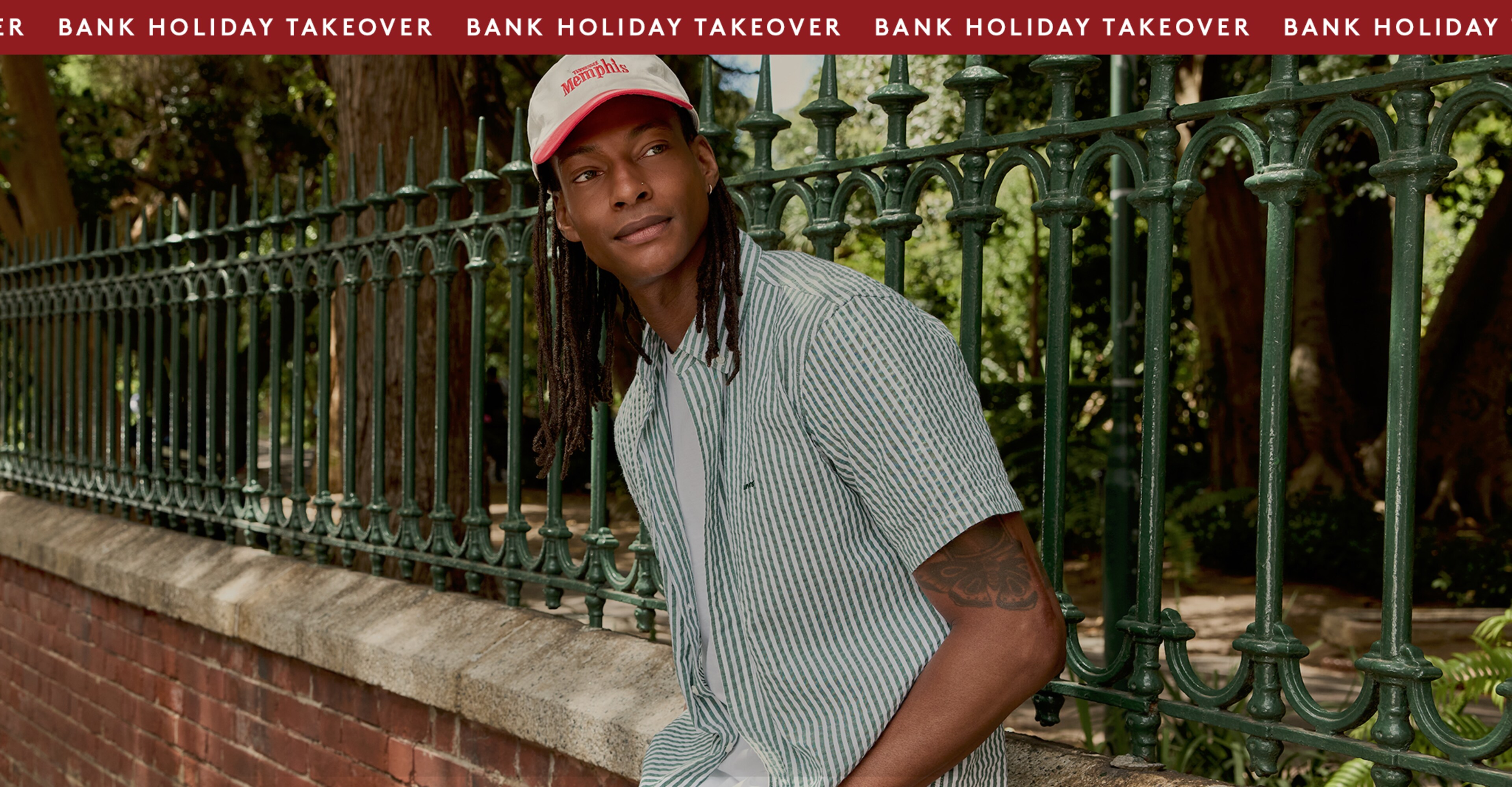 Model is wearing a Levi's green stripe short sleeve button down shirt with a cream and red cap.