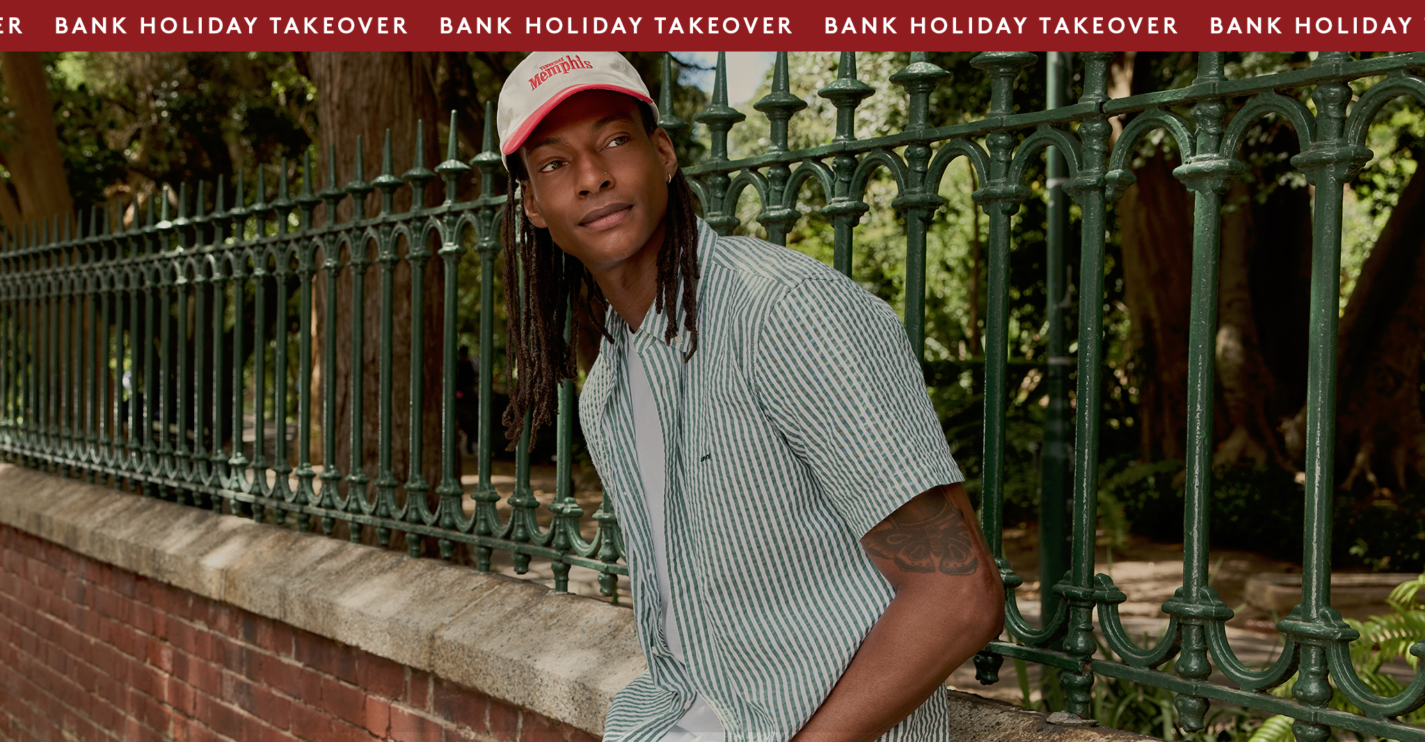 Model is wearing a Levi's green stripe short sleeve button down shirt with a cream and red cap.