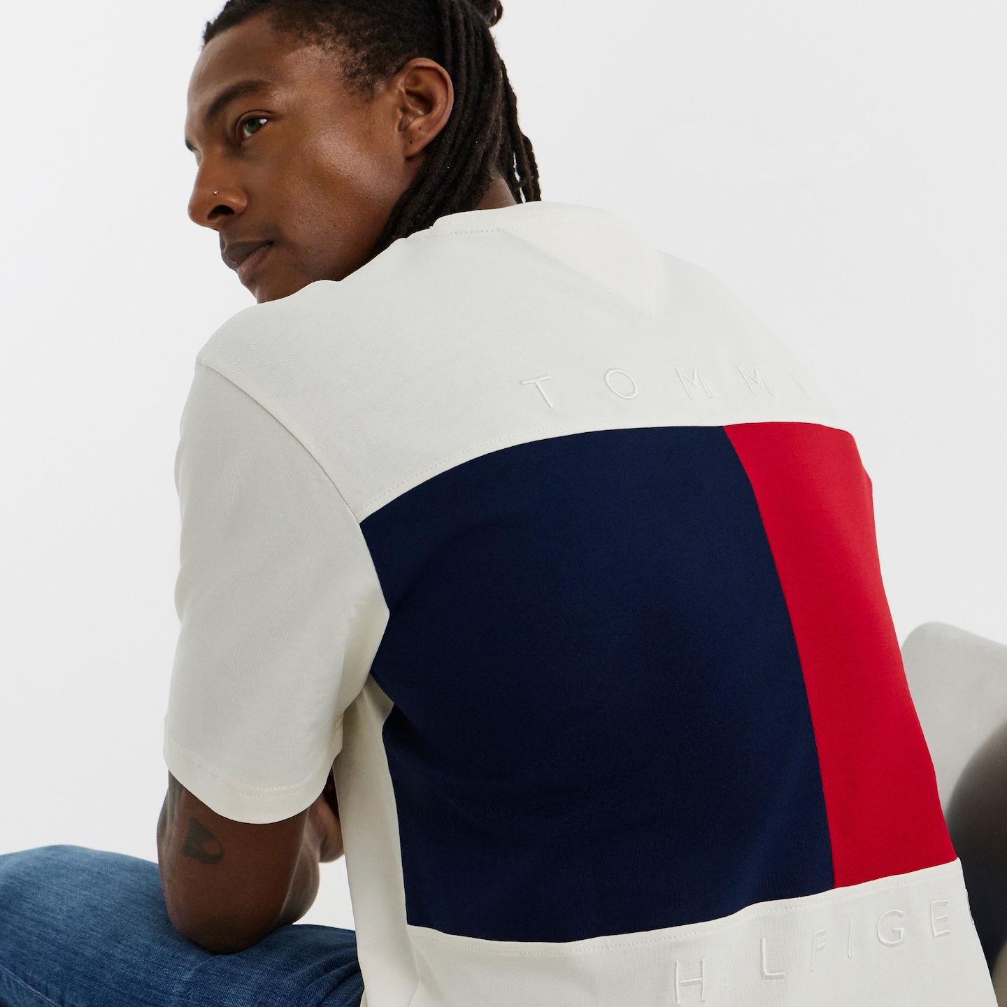 Model is wearing a white Tommy Hilfiger short sleeve back flag t-shirt with a pair of jeans.