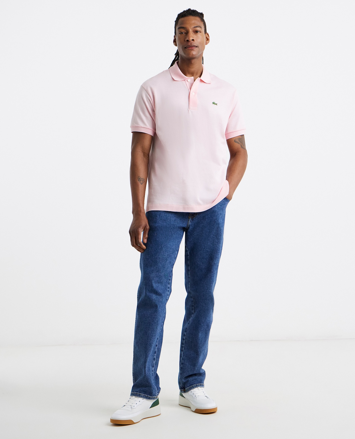Model is wearing a light pink Lacoste Classic short sleeve pique polo with a pair of blue jeans and trainers.