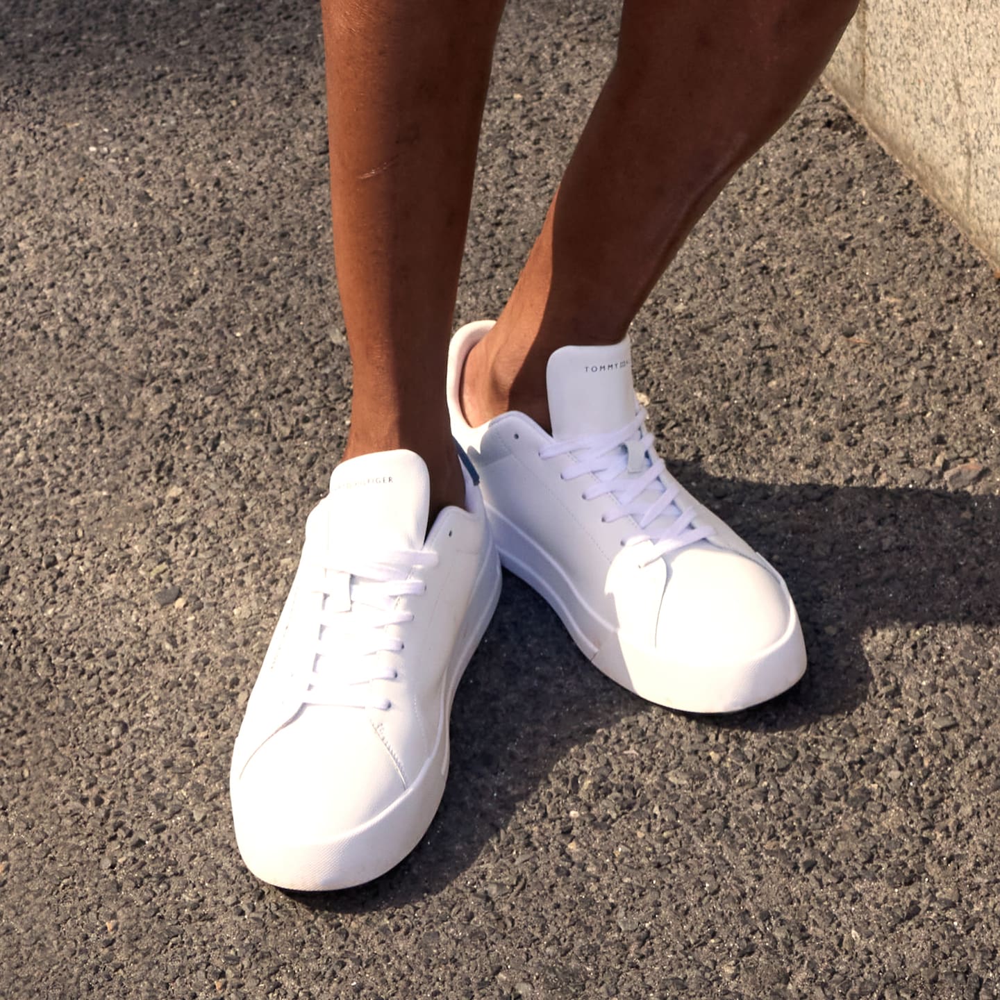 Model is wearing a pair of white Tommy Hilfiger trainers.