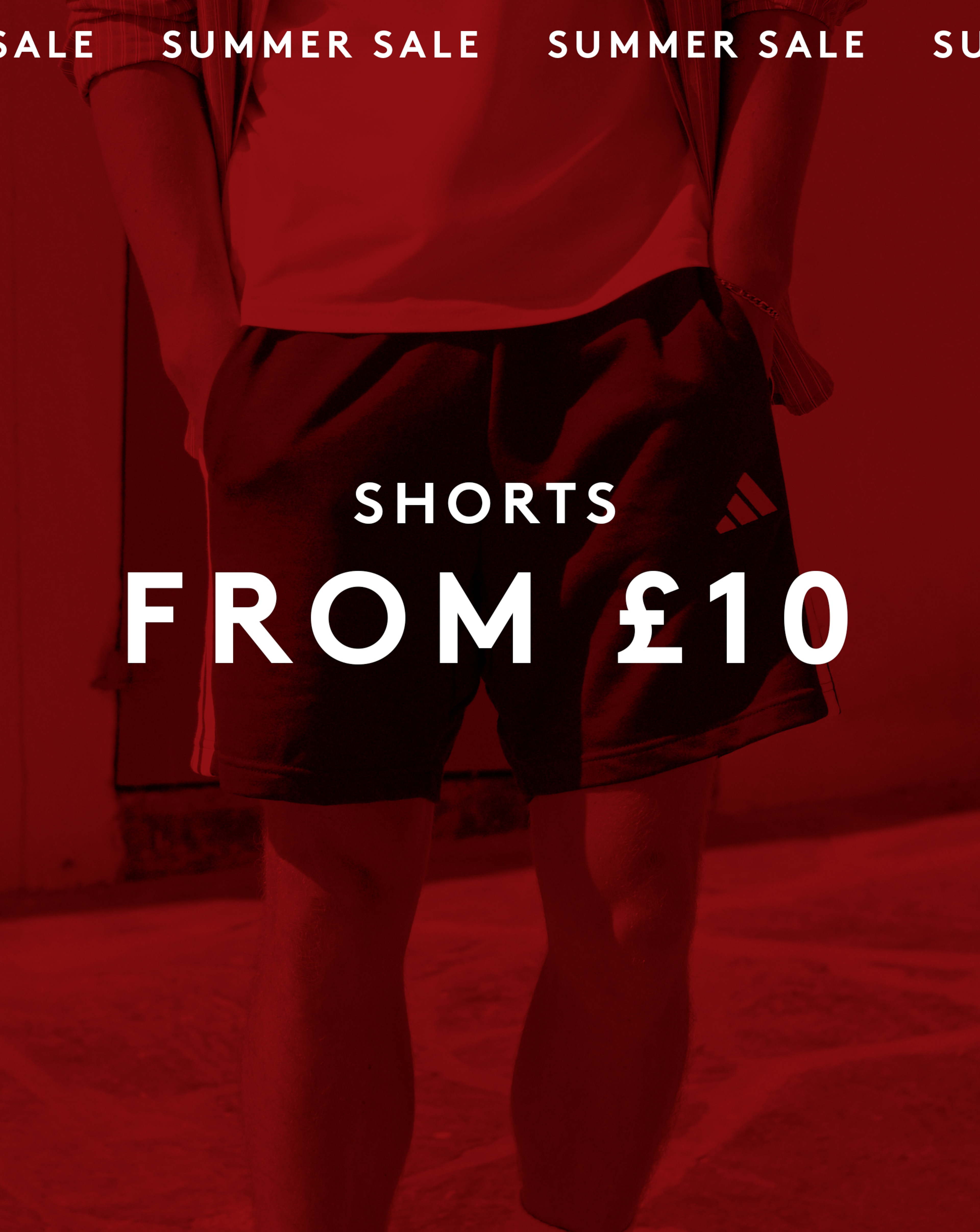 Shorts From £10. Model wears adidas 3 Stripes French Terry Shorts behind red sale back drop