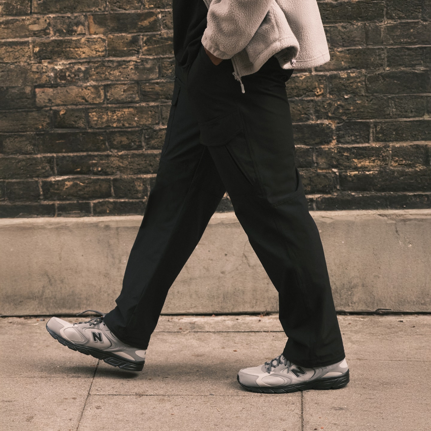 A person walking from right to left wearing dark trousers and grey trainers.