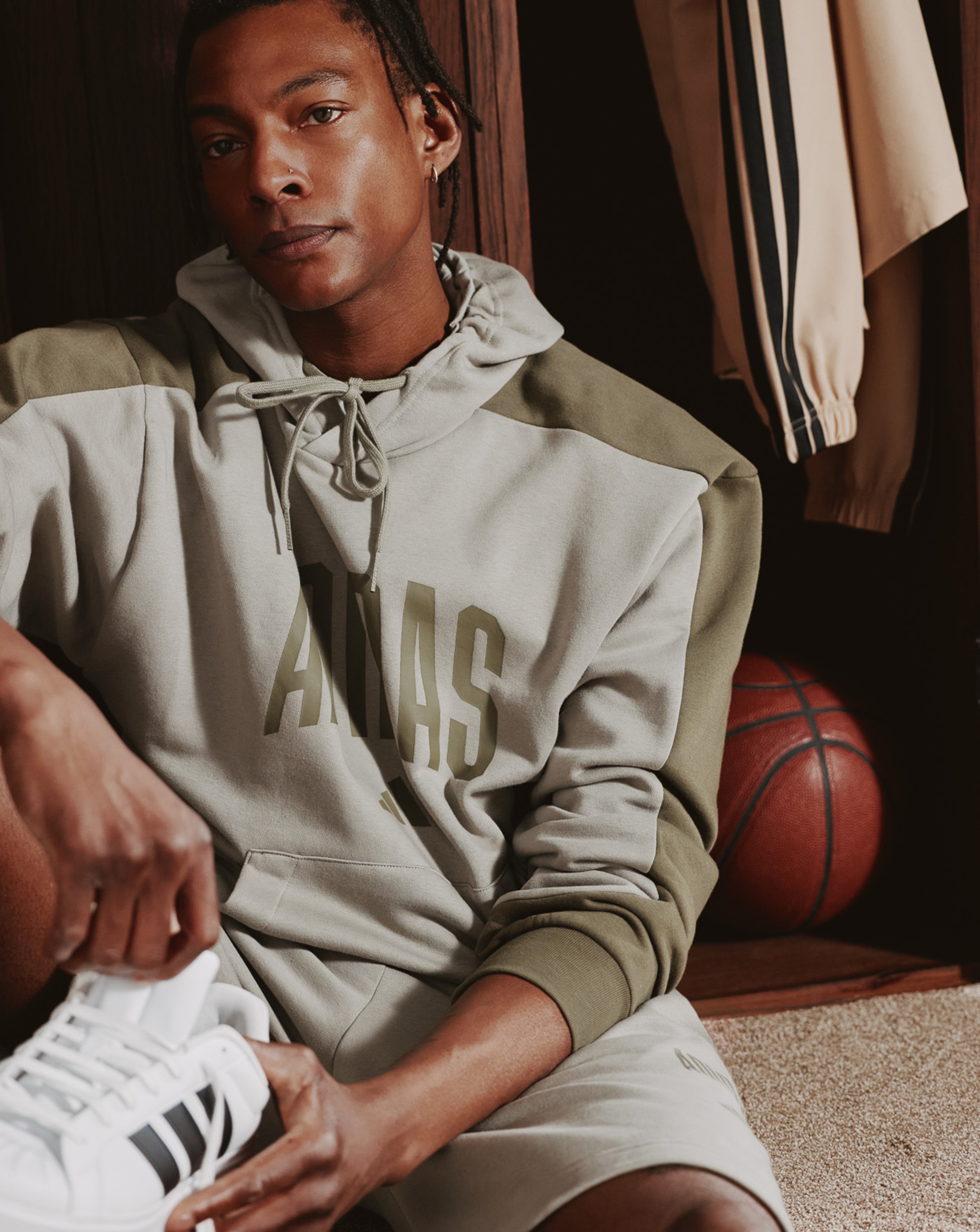 Model wears adidas Collegiate Hoodie sat in sports changing room.