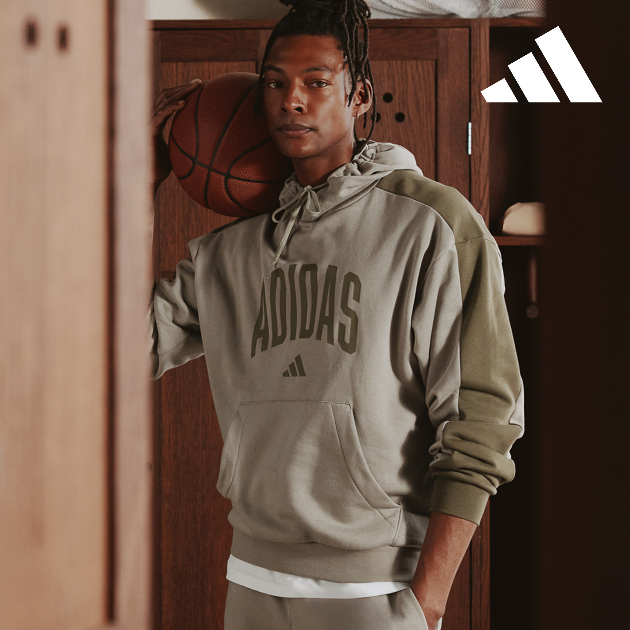 Model shown through locker holding basket ball wears adidas Collegiate Hoodie in Pale Olive.