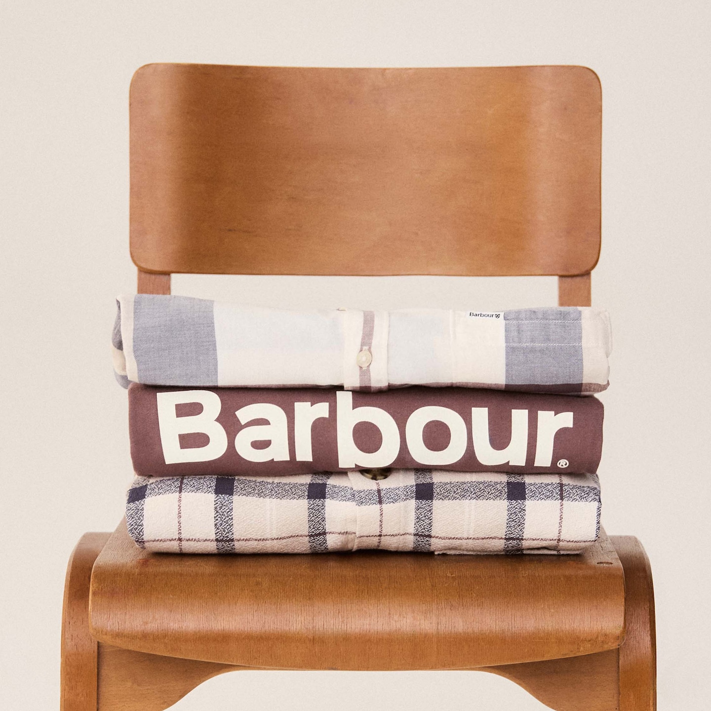 A pile of sdhirts and sweatshirts folded on a chair.