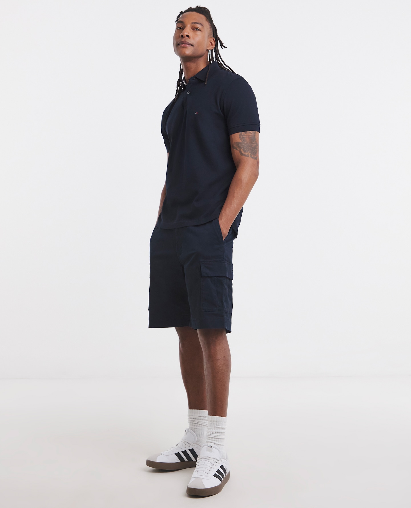 Model is wearing Tommy Hilfiger River navy cargo shorts with a navy polo shirt and a pair of adidas trainers.