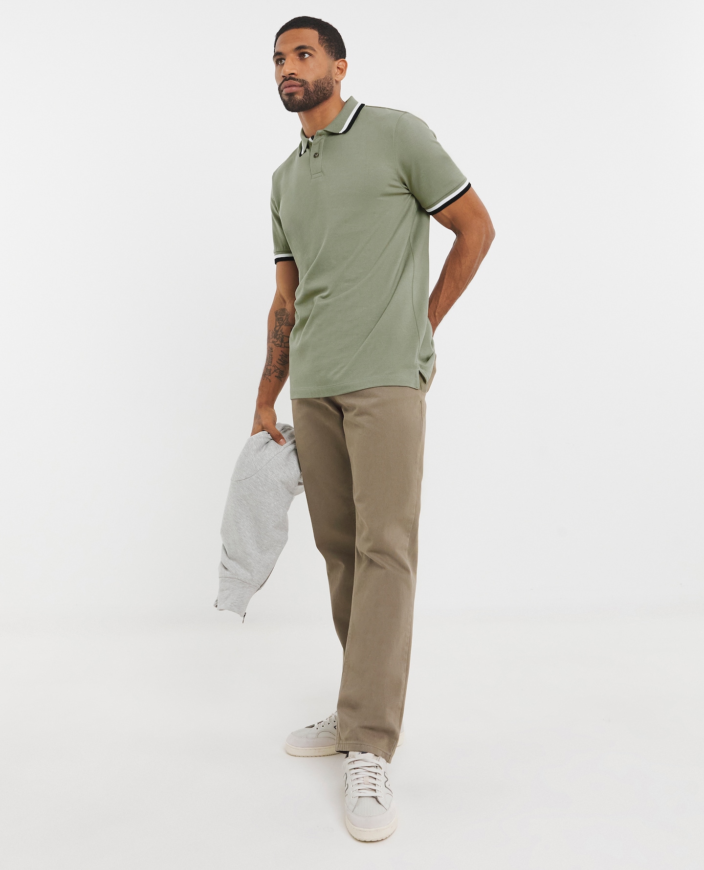 Model is wearing a Tipped Pique polo khaki t-shirt with a pair of chinos and trainers.
