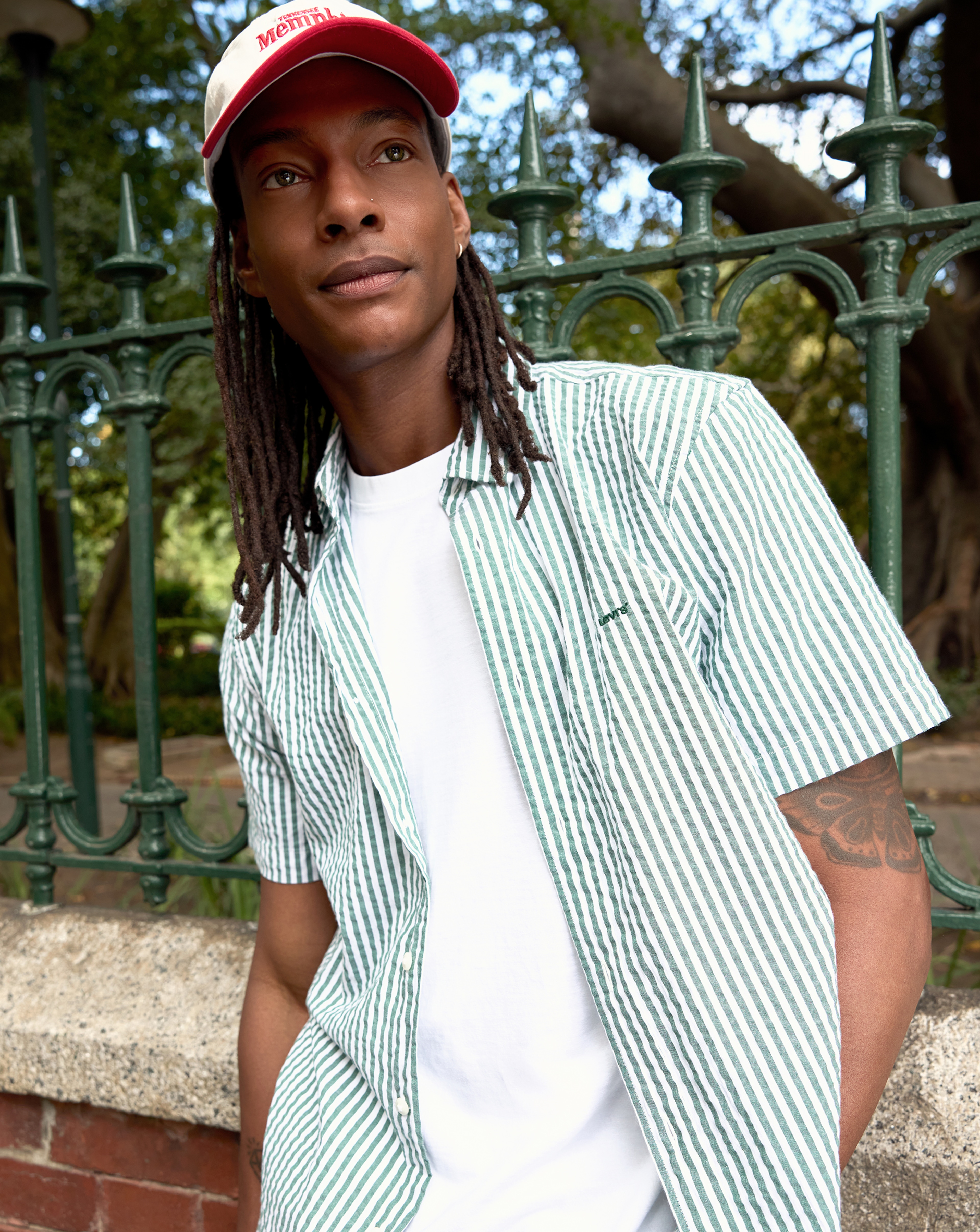 Model is wearing a Levi's short sleeve green stripe shirt  over a white t-shirt with a red and white cap.