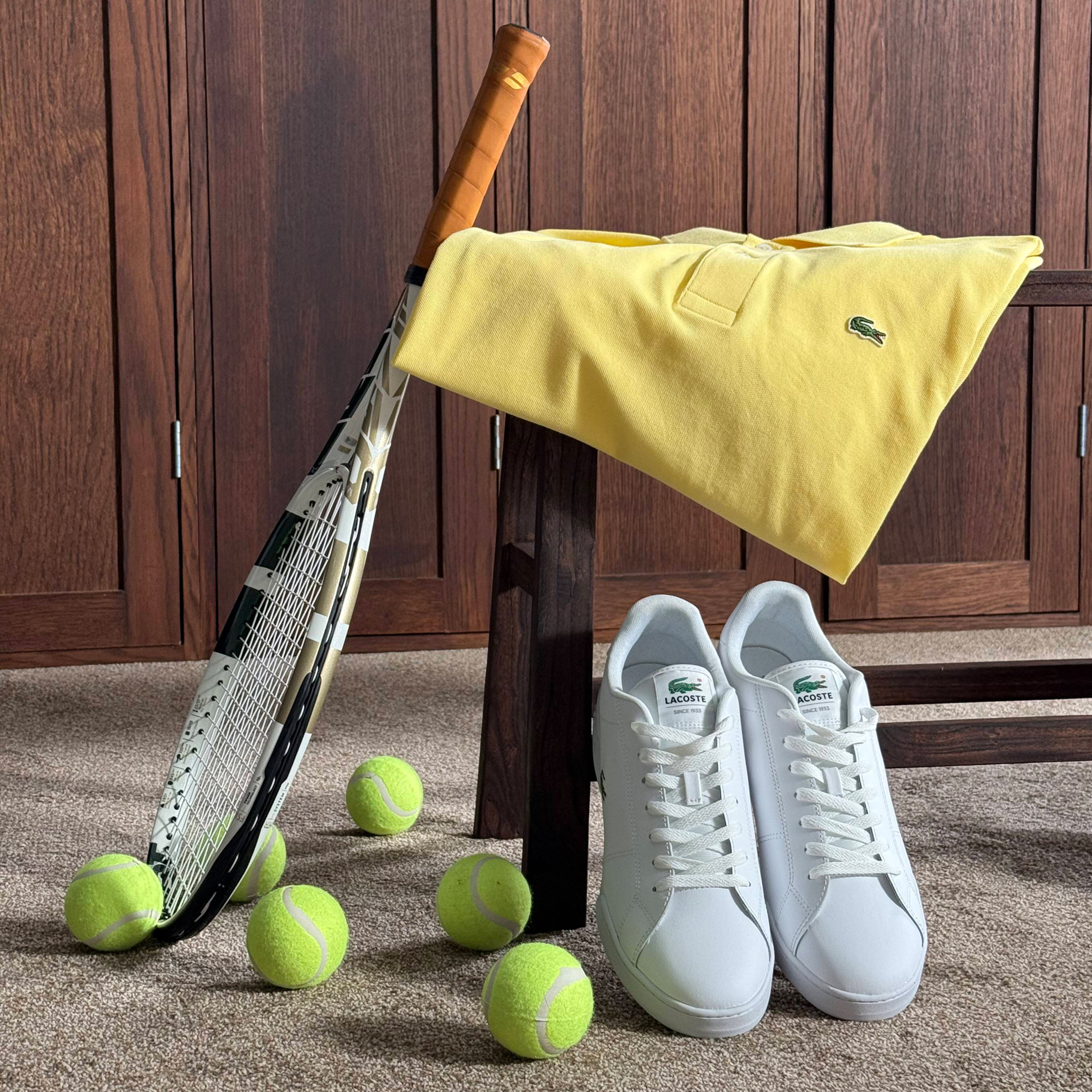 Lacoste Classic Short Sleeve Pique Polo - Yellow with Lacoste Carnaby Cup Leather Trainer - White pictured with tennis racket and tennis balls