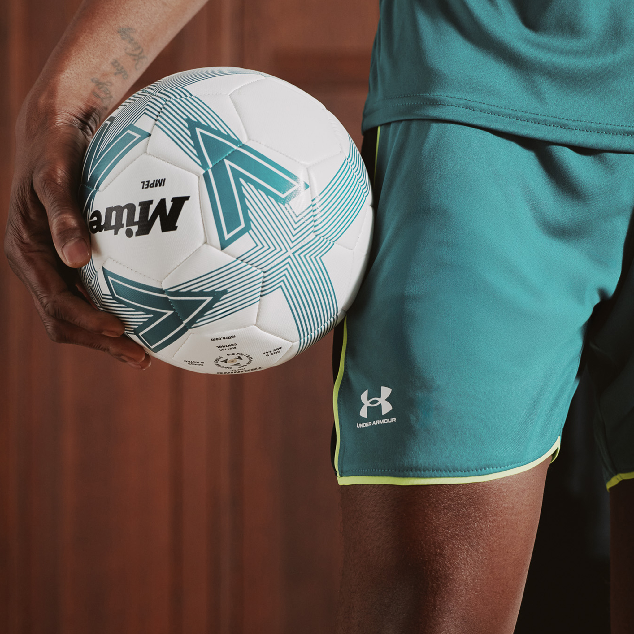 Model is wearing Under Armour Challenger train t-shirt with matching shorts holding a football.