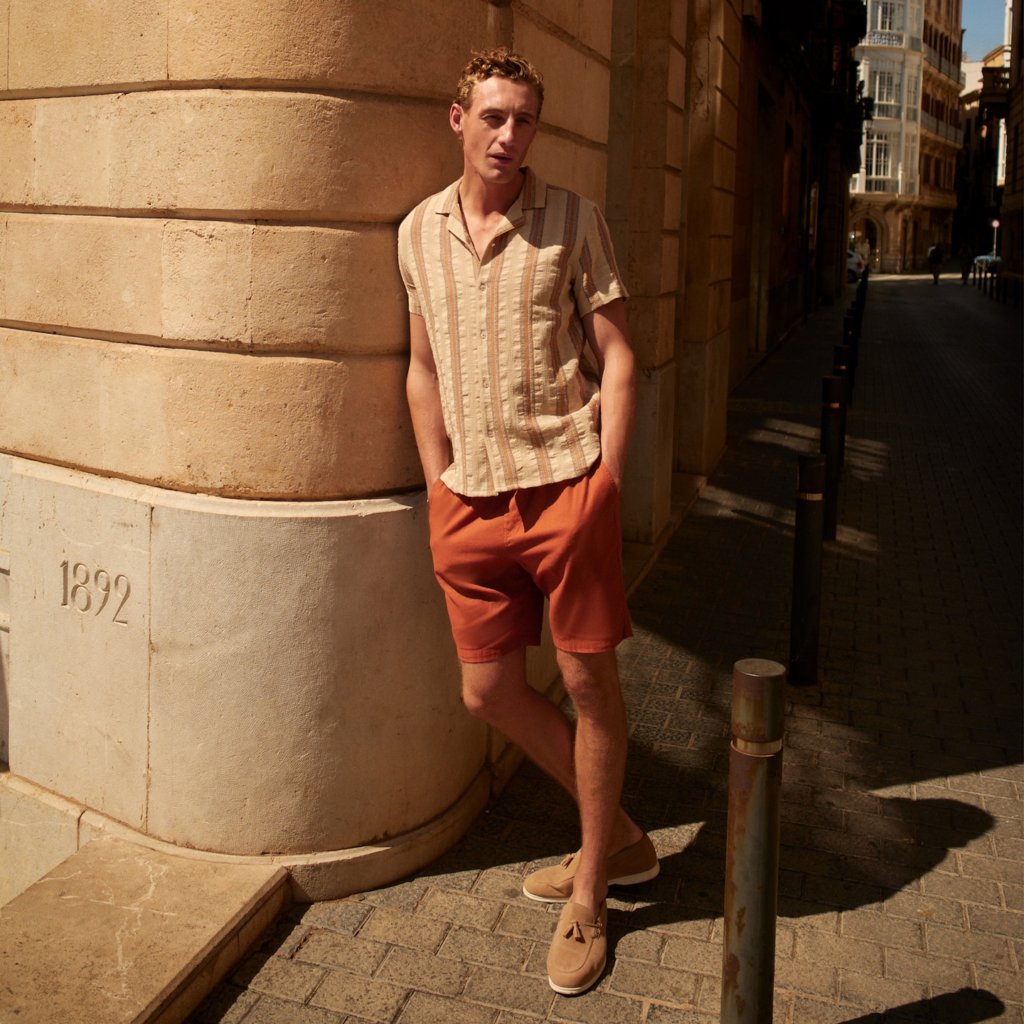 Model stood on a European street wearing pink shorts and linen striped shirt