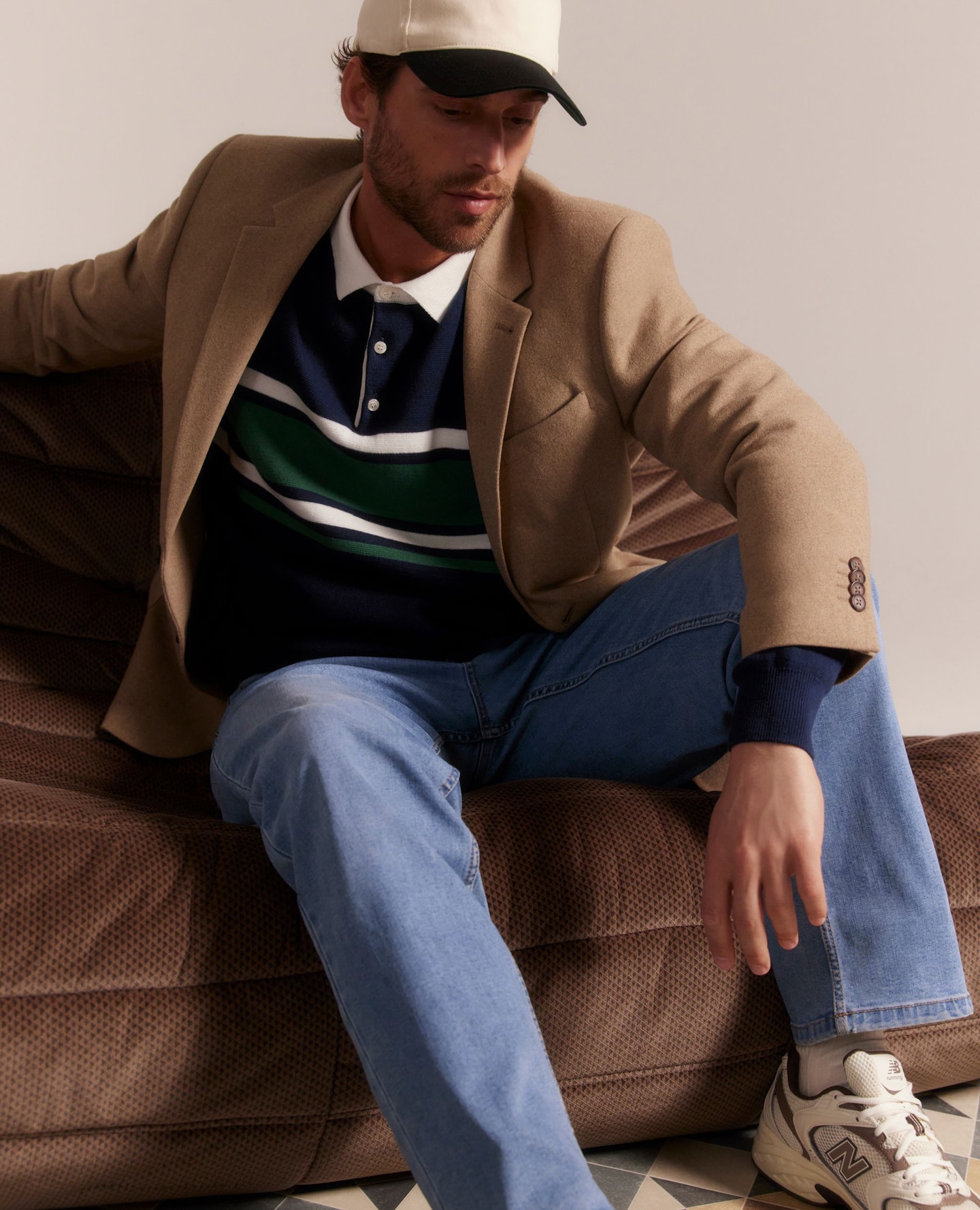 Model wearing beige jacket, blue and white striped rugby top, blue jeans and New Balance.