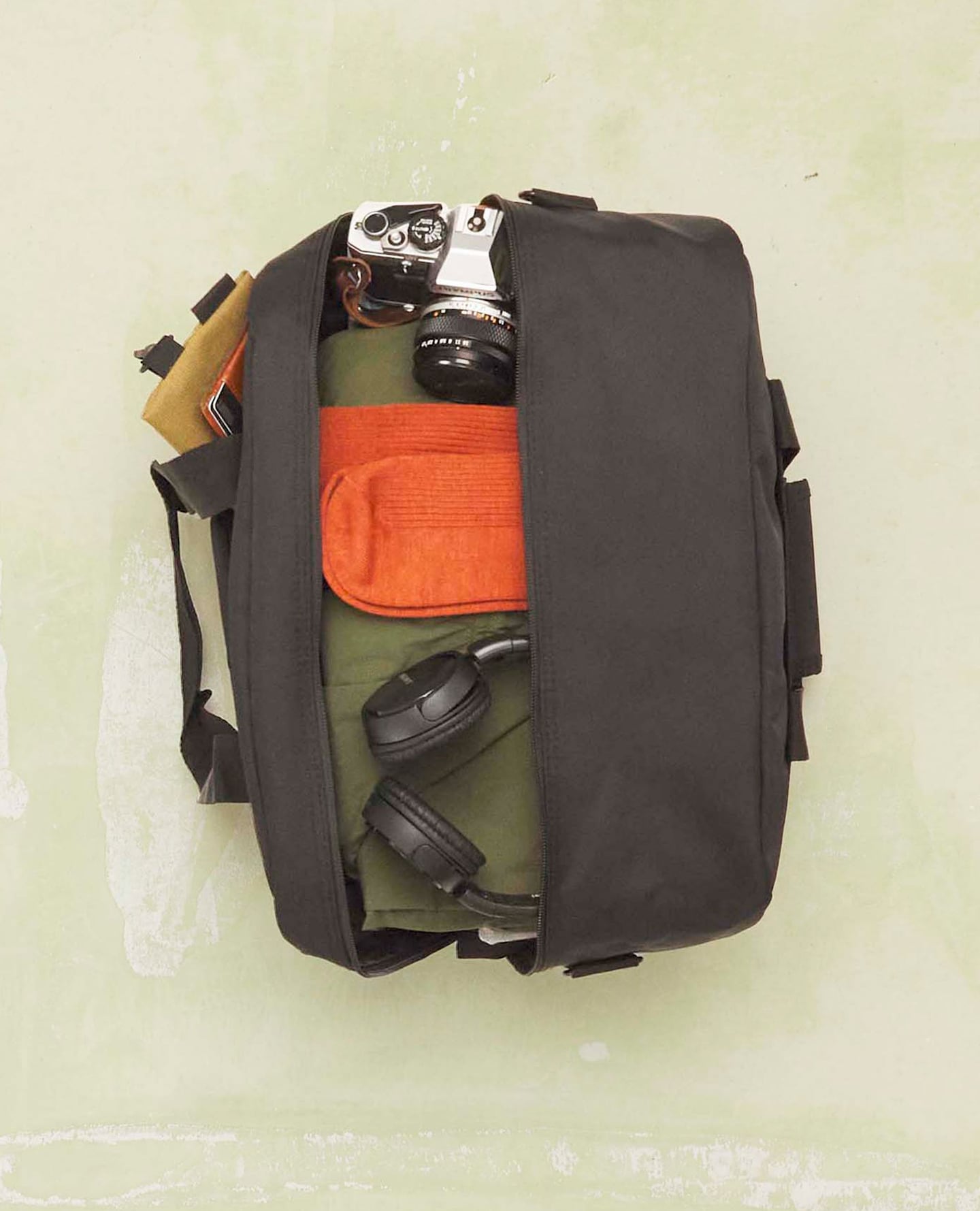 Travel bag is packed, open revealing some travel related tech. Camera and wireless headphones.