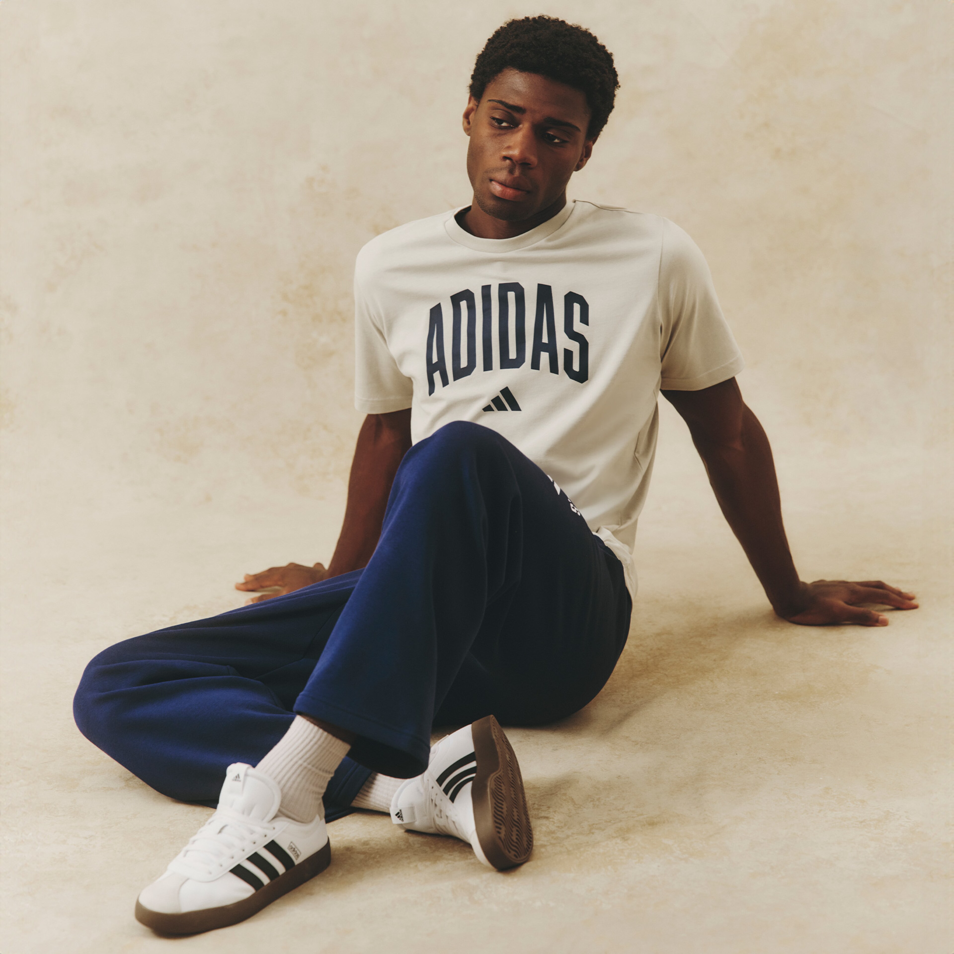 Model wearing white adidas logo tee and adidas navy blue tracksuit bottoms