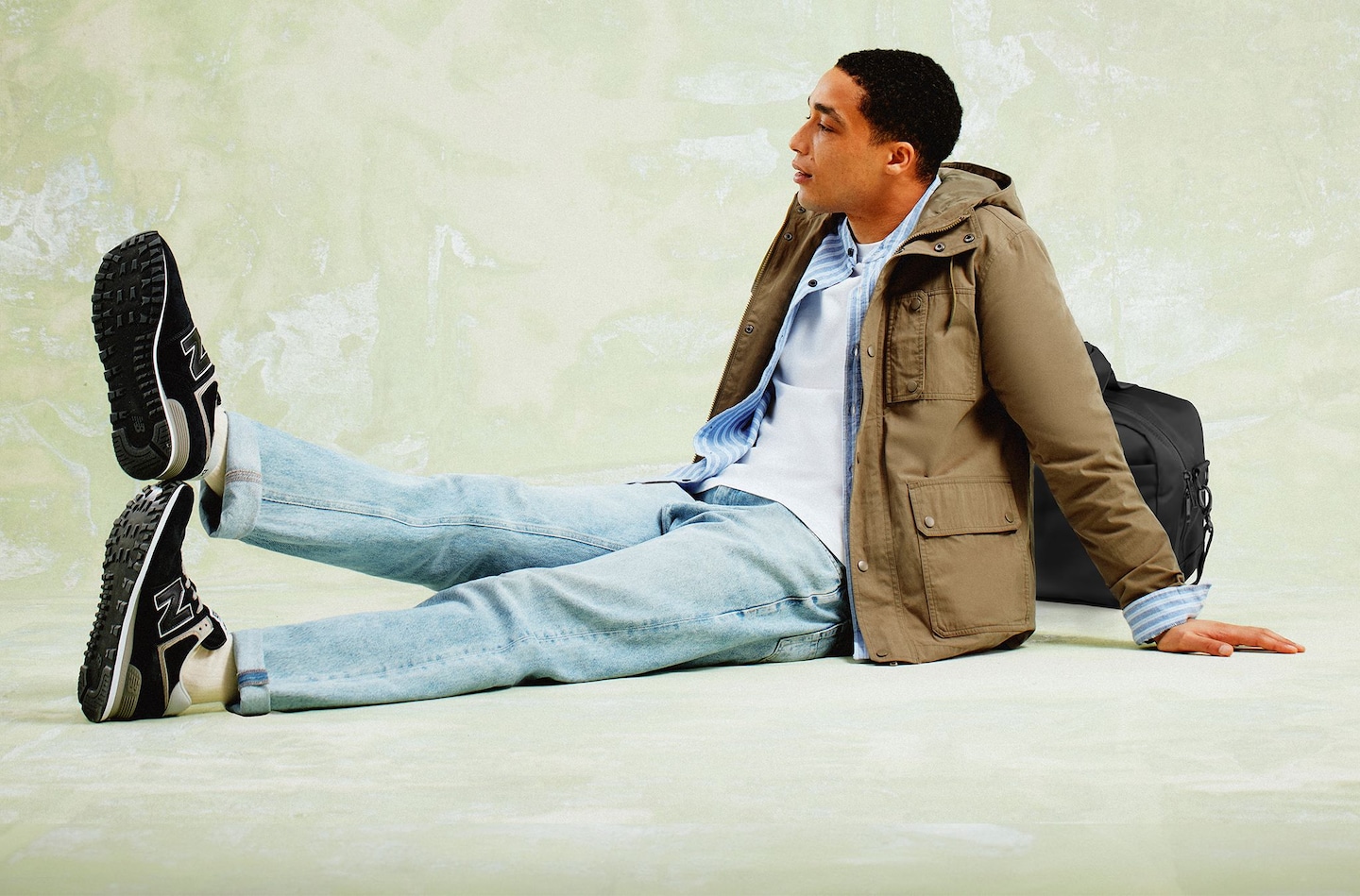 Model is sat down and wearing travel clothes / has travel bag