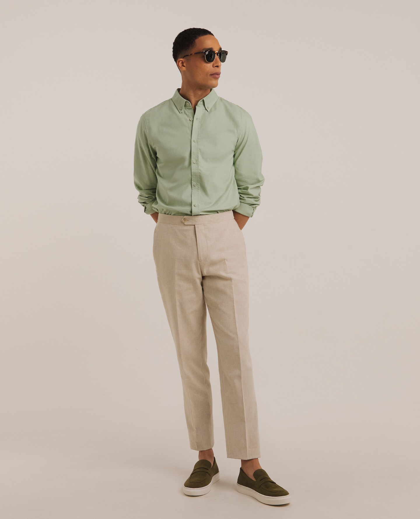 Model wearing sunglasses, green shirt and cream trousers