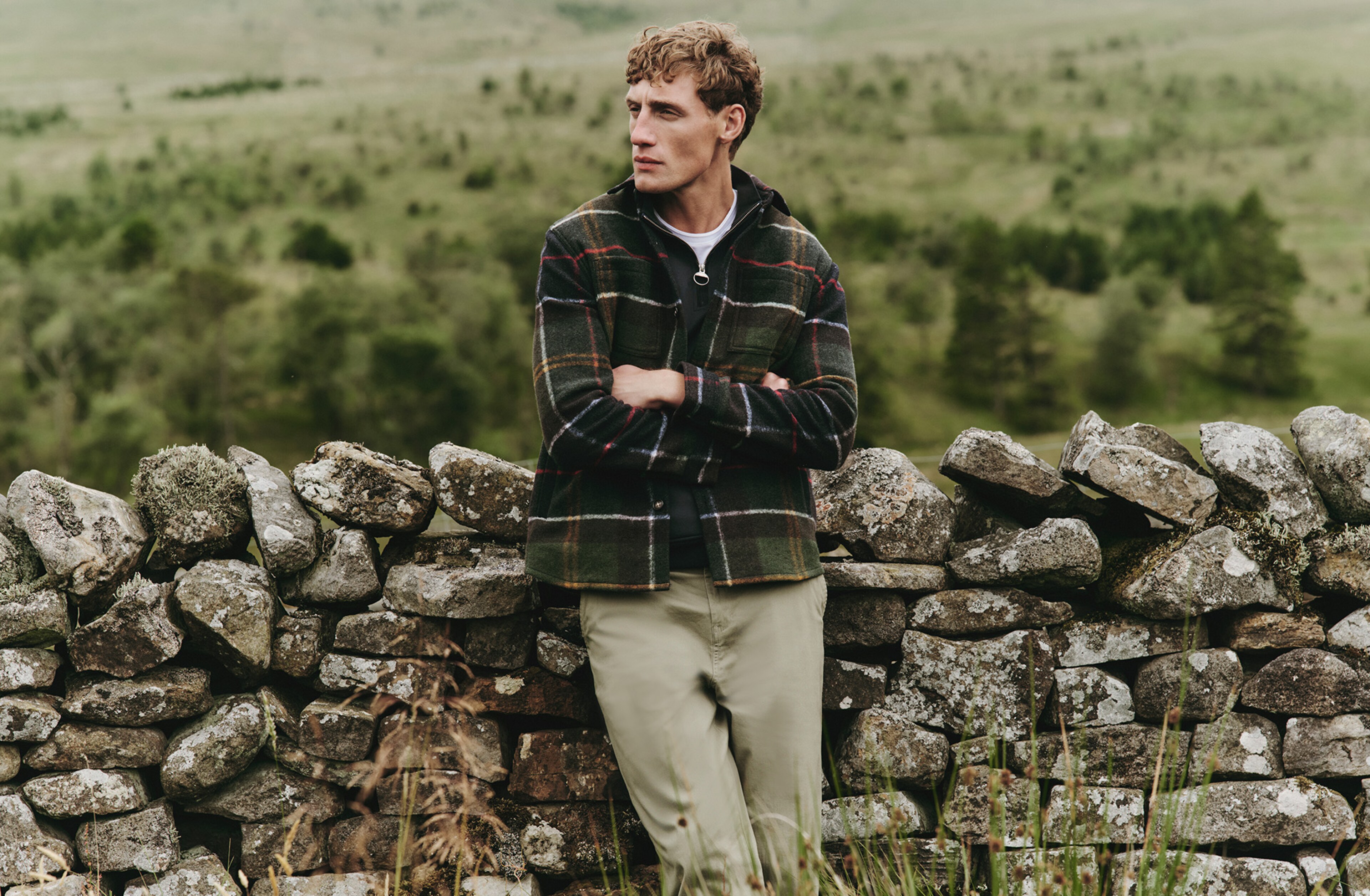 Model in the countryside wearing a checkered Barbour jacket and Barbour trousers