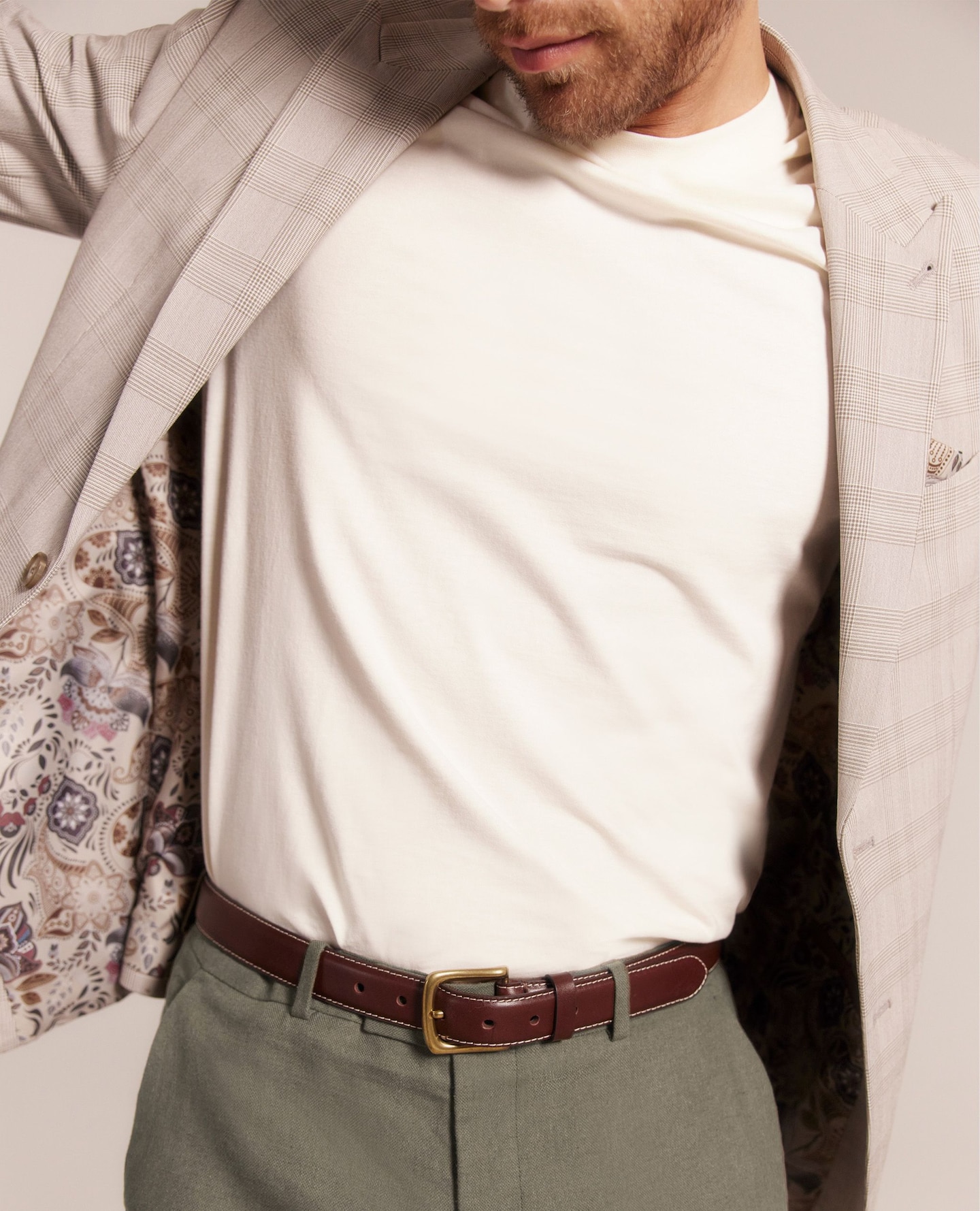 Model wearing a light beige suit jacket, a white t-shit, brown belt and khaki suit trousers