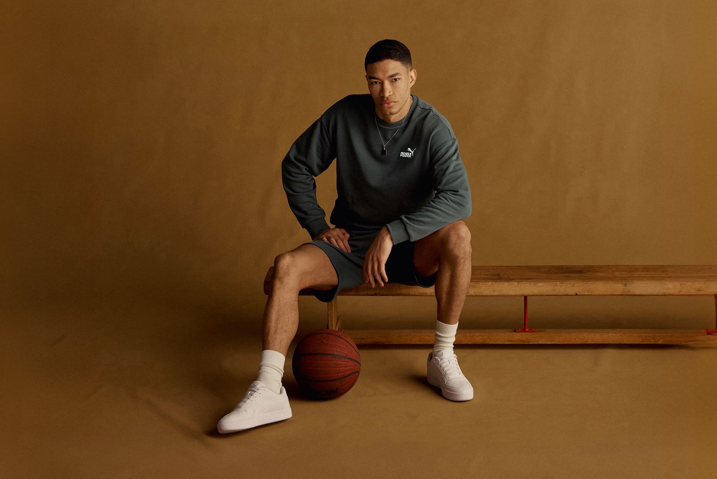 Model sat on Gym bench with basket ball wears green Puma sports top and shorts