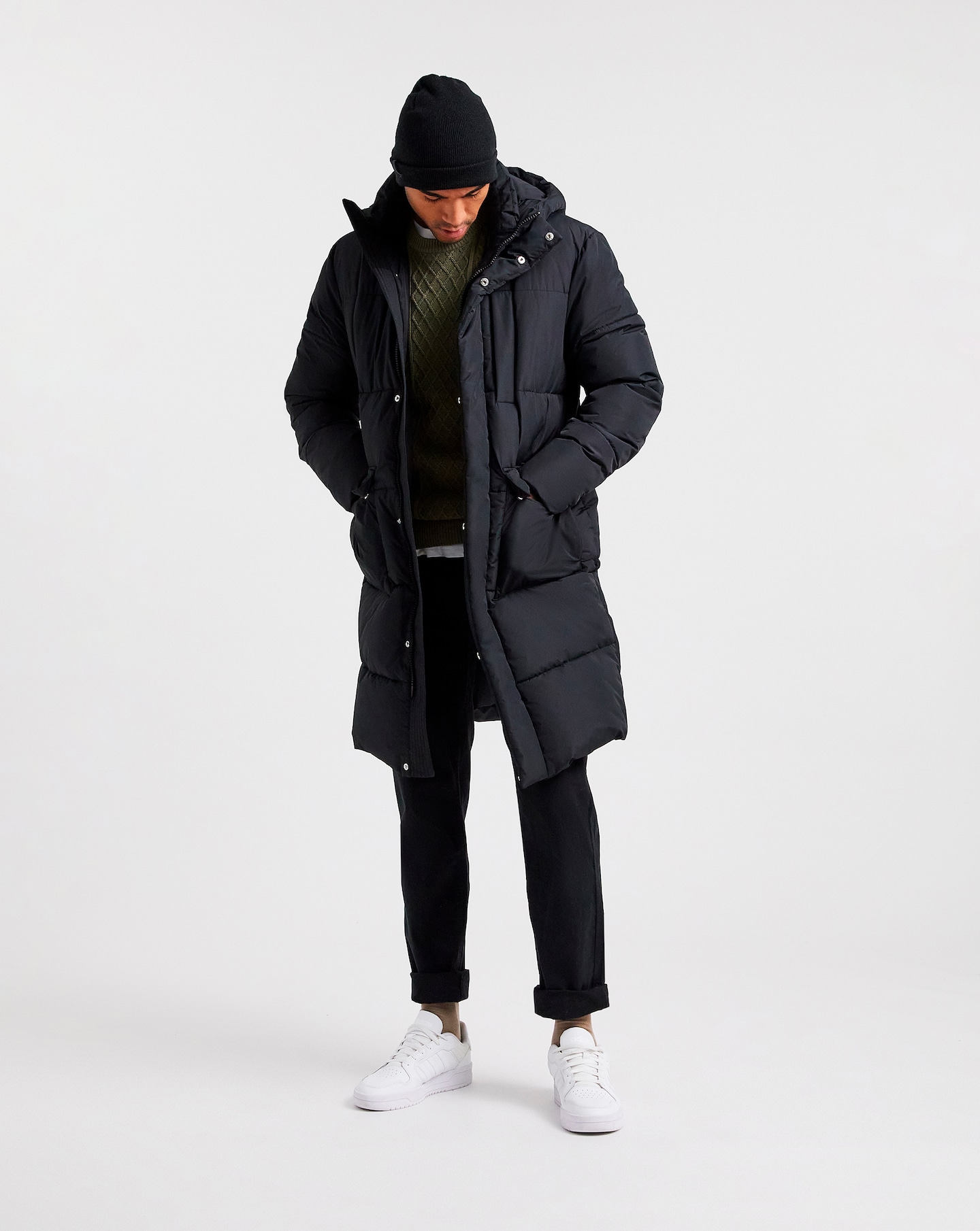 A man stood up looking down at his feet wearing a longline padded coat.