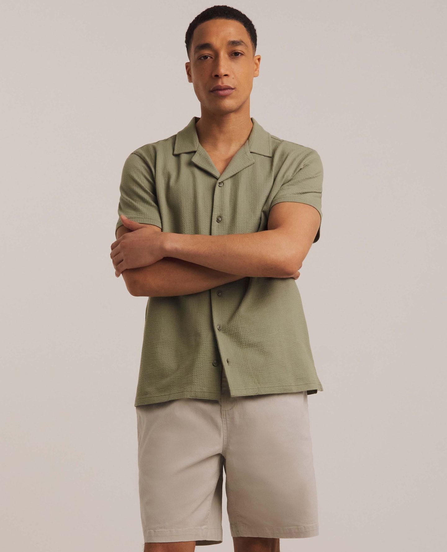 Model wearing green button up t-shirt and beige shorts