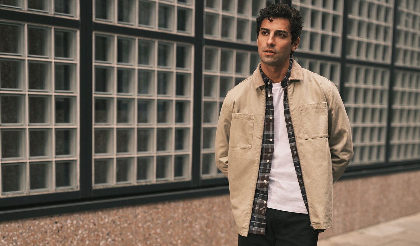 Model wears cream jacket, stood again a lamppost in thought.