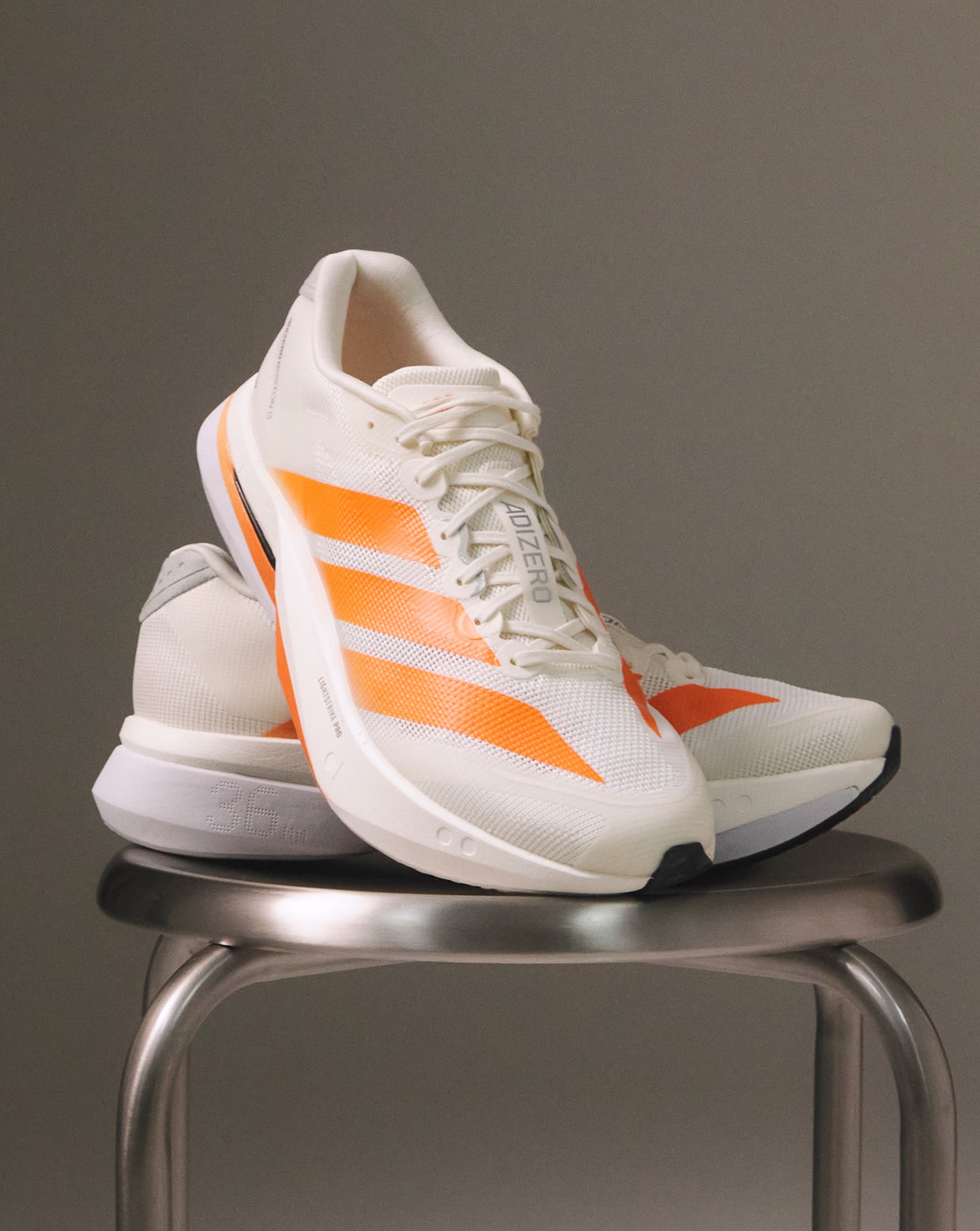 A pair of orange and white adidas Adizero Boston 13 trainers on a silver stool