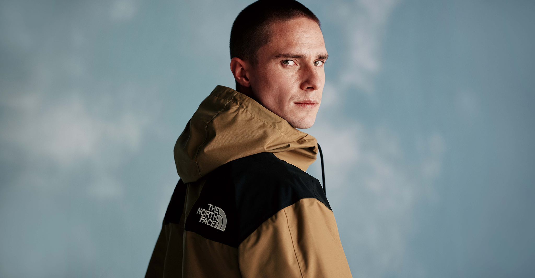 The North Face. Model wears Reign On Jacket in Cedar-TNF Black against sky blue background.