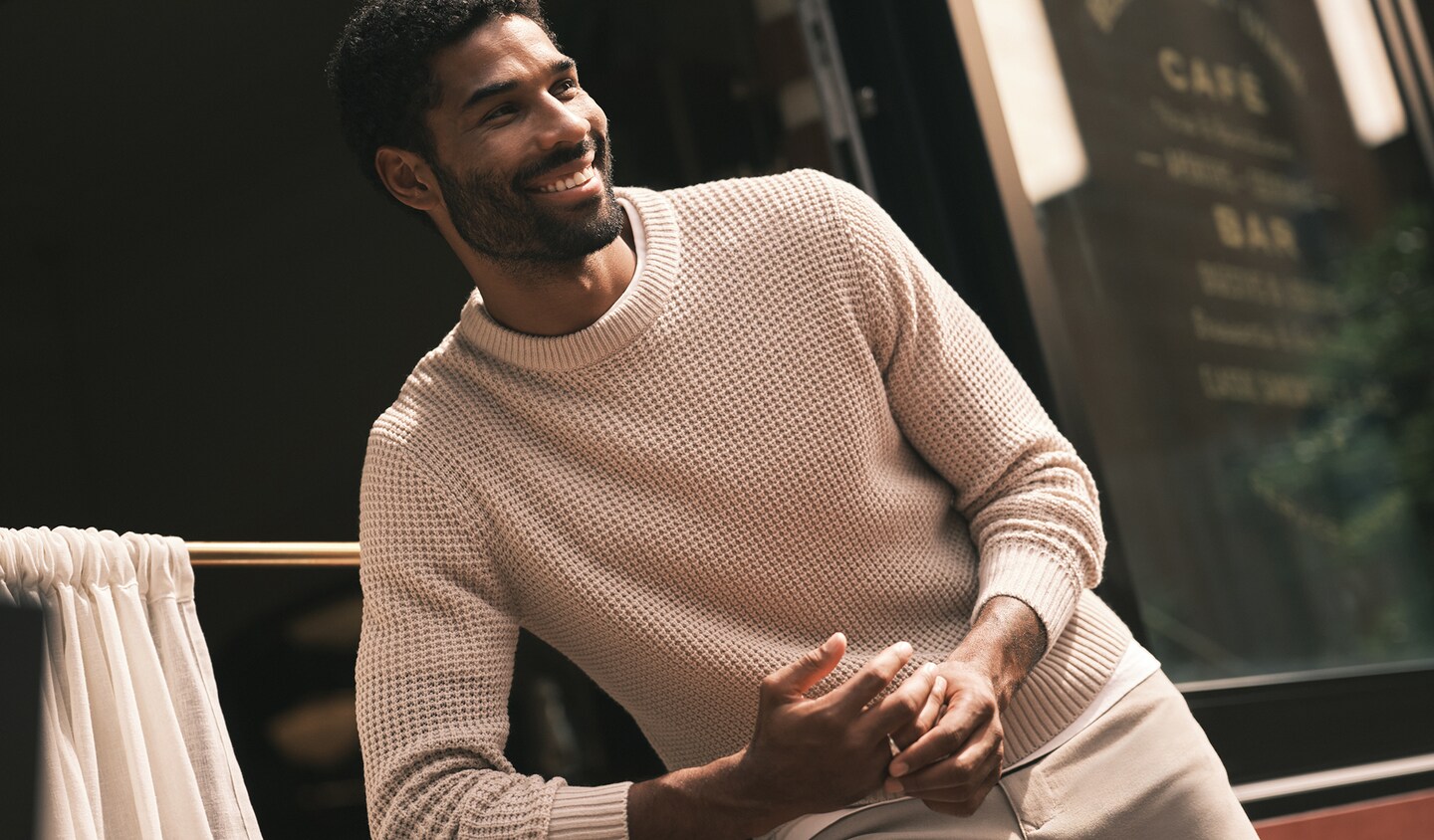 Model wears cream jumper and is sat outside a cafe