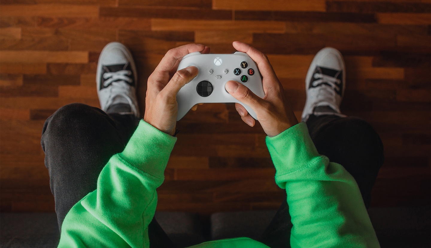 A person playing on an Xbox with a light grey controller wearing a green jumper