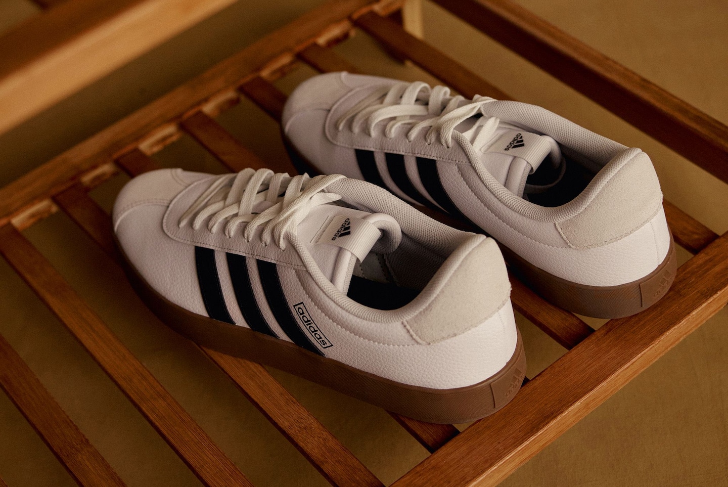 Pair of white adidas court trainers on a wooden rack