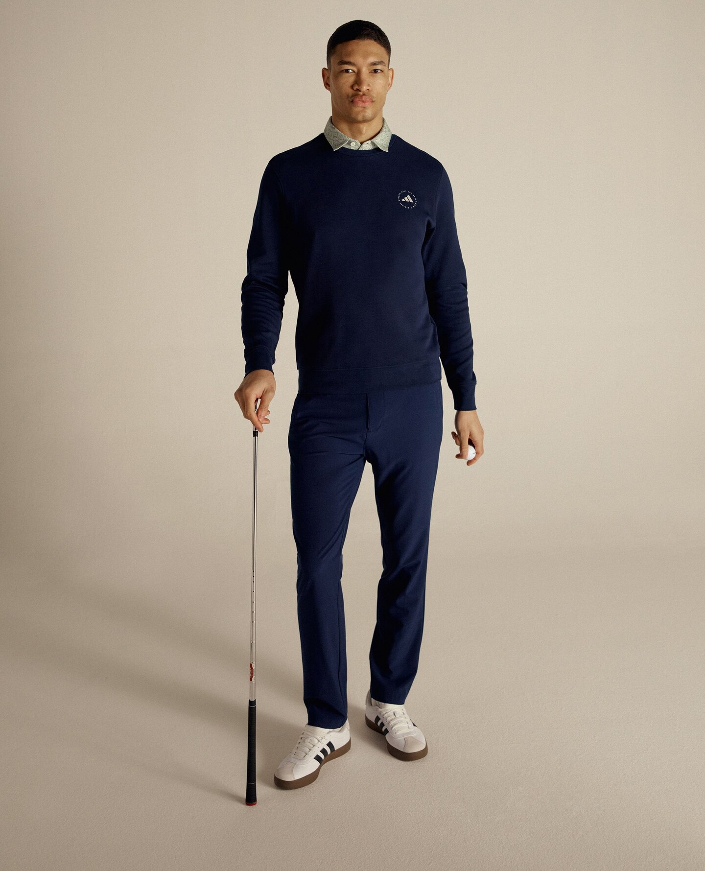 Golfing model is stood wearing navy adidas jumper with navy trousers and adidas trainers