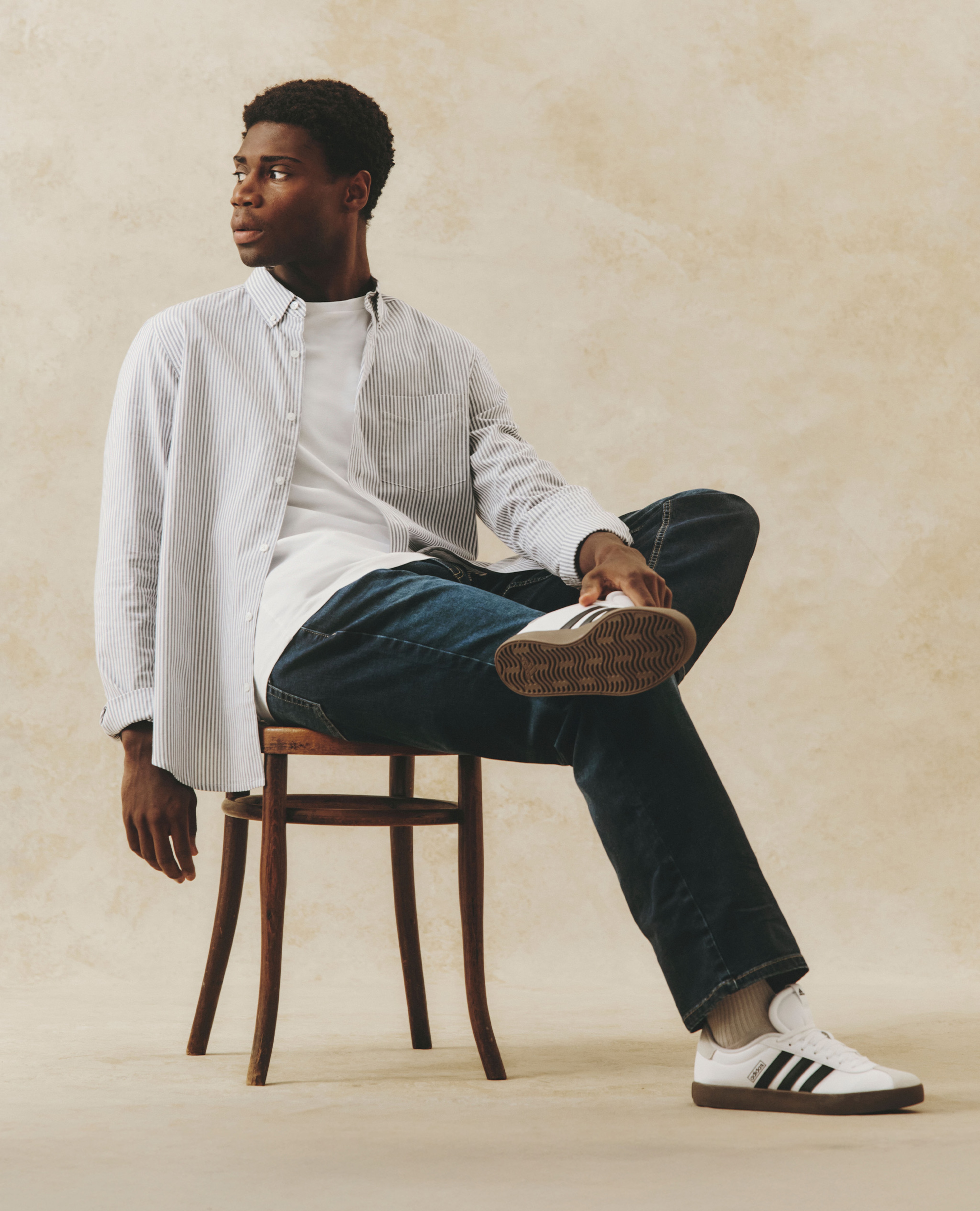 Model wearing striped shirt with a white t-shirt, jeans and adidas trainer