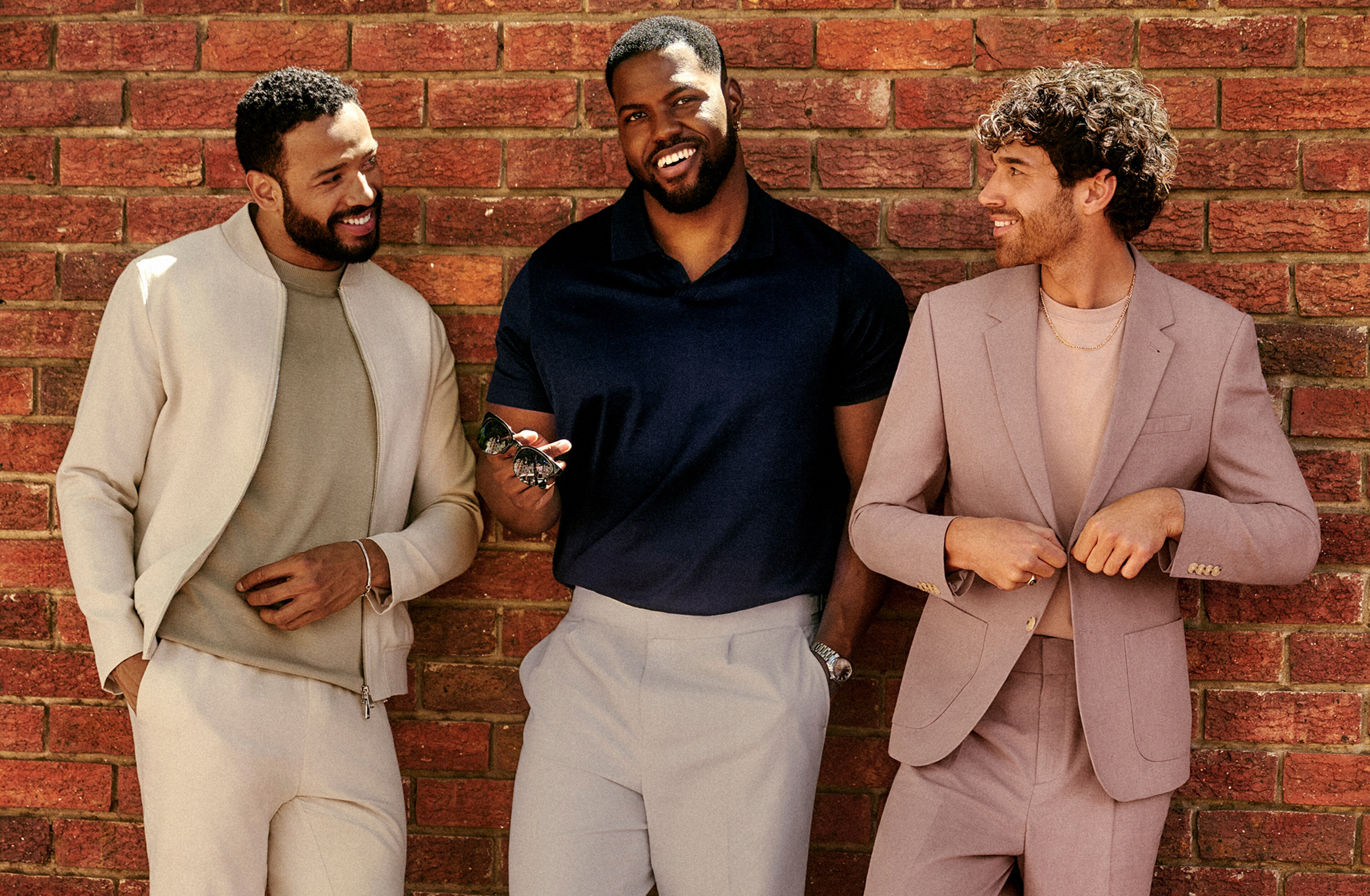 3 models sat in a row wearing Linen Blend suit in dusty pink, Black shirt and Linen trousers and Tailored Linen Bomber with cream trousers