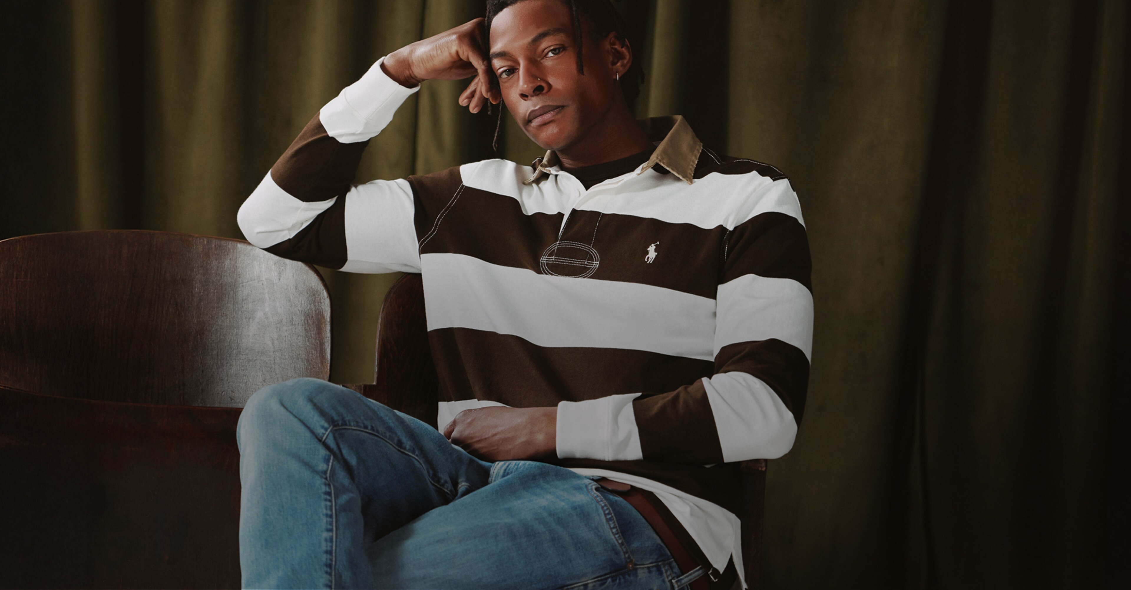 Model is wears Polo Ralph Lauren Long Sleeve Stripe Rugby - Brown/Cream sat against a dark green curtain back drop.