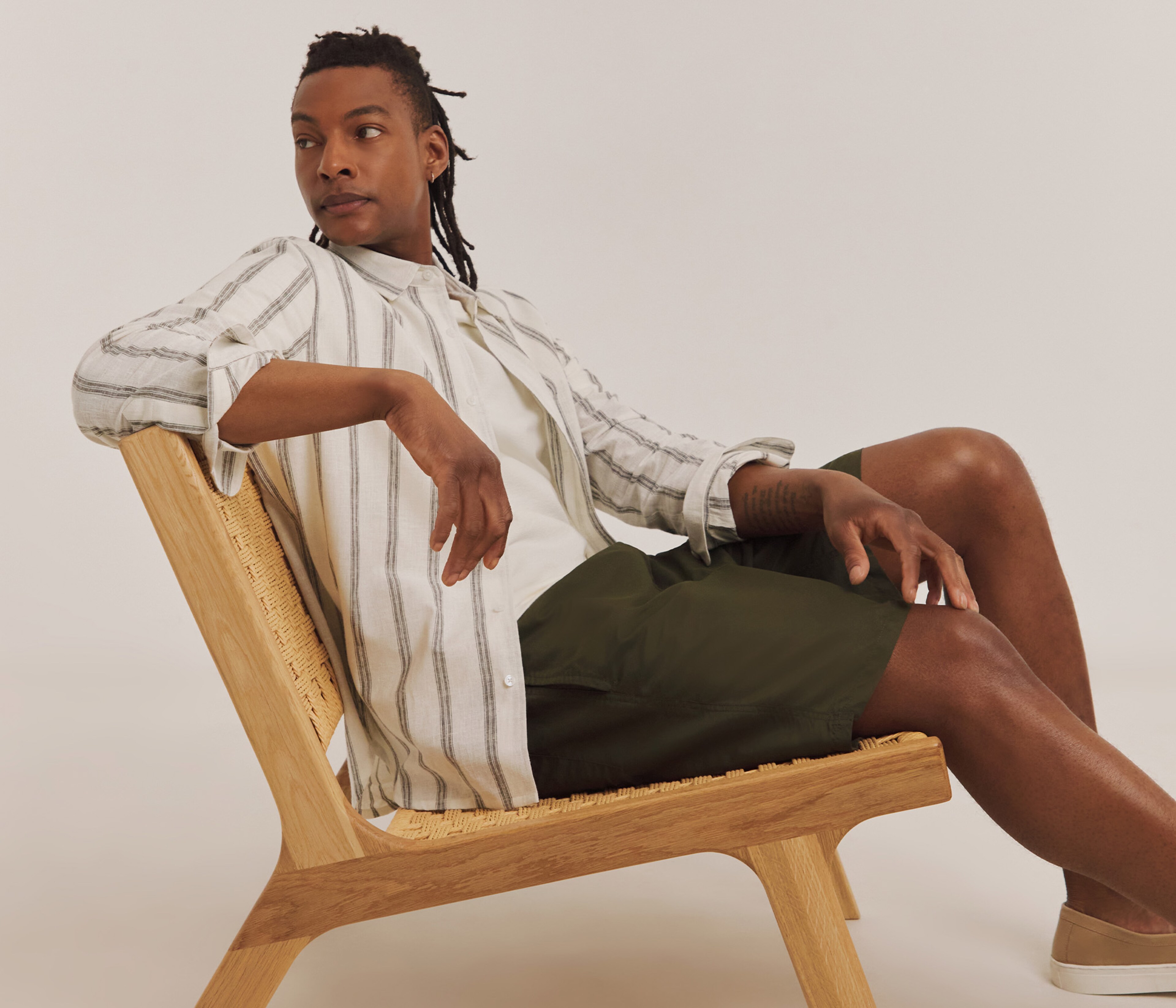 Model sat on chair wearing khaki shorts and a striped shirt