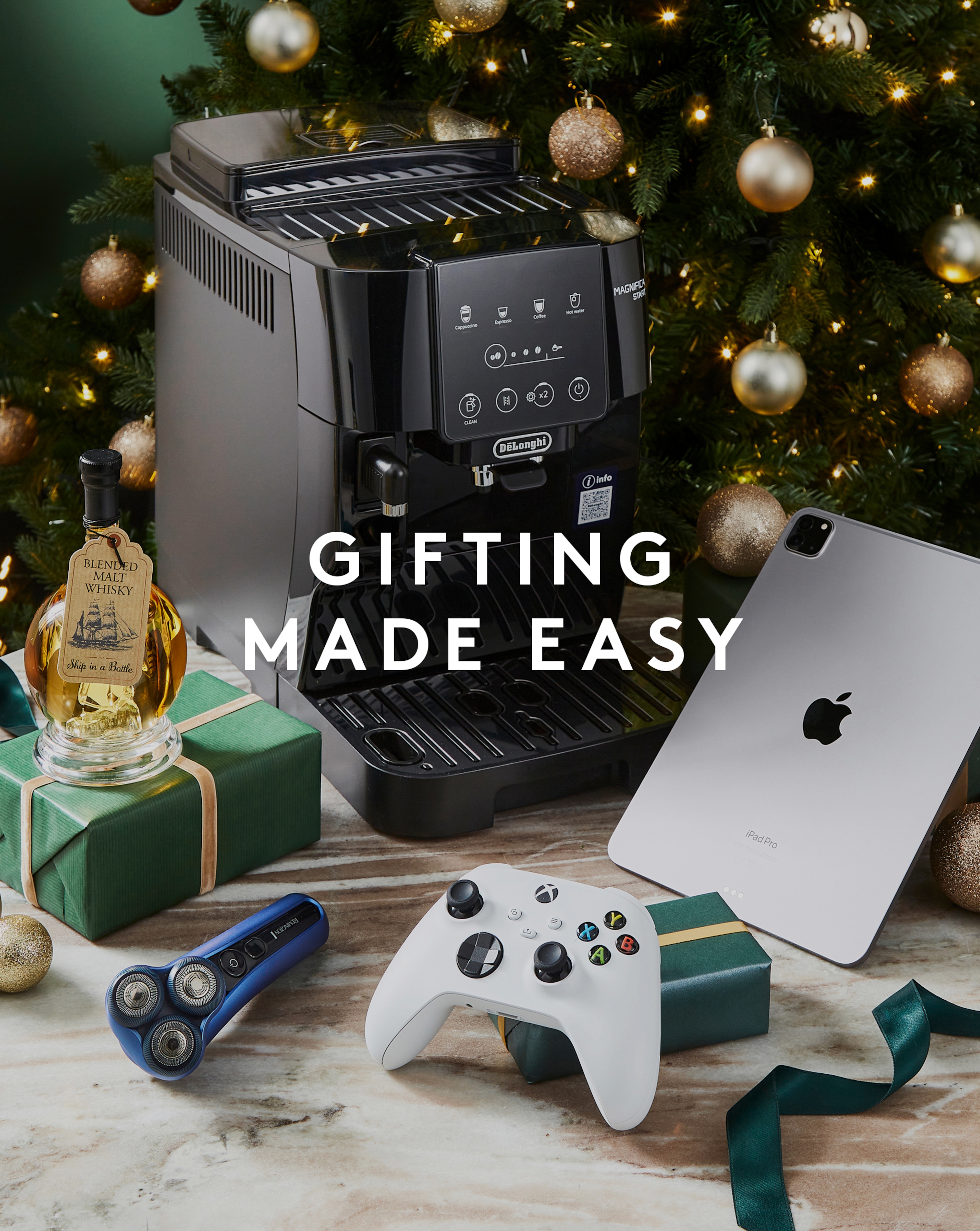 Gifting made easy. Products displayed in front of Christmas tree include De'Longhi Coffee Machine, PS5 Controller, Remmington Shaver, IPad and Blended Malt Whisky Ship